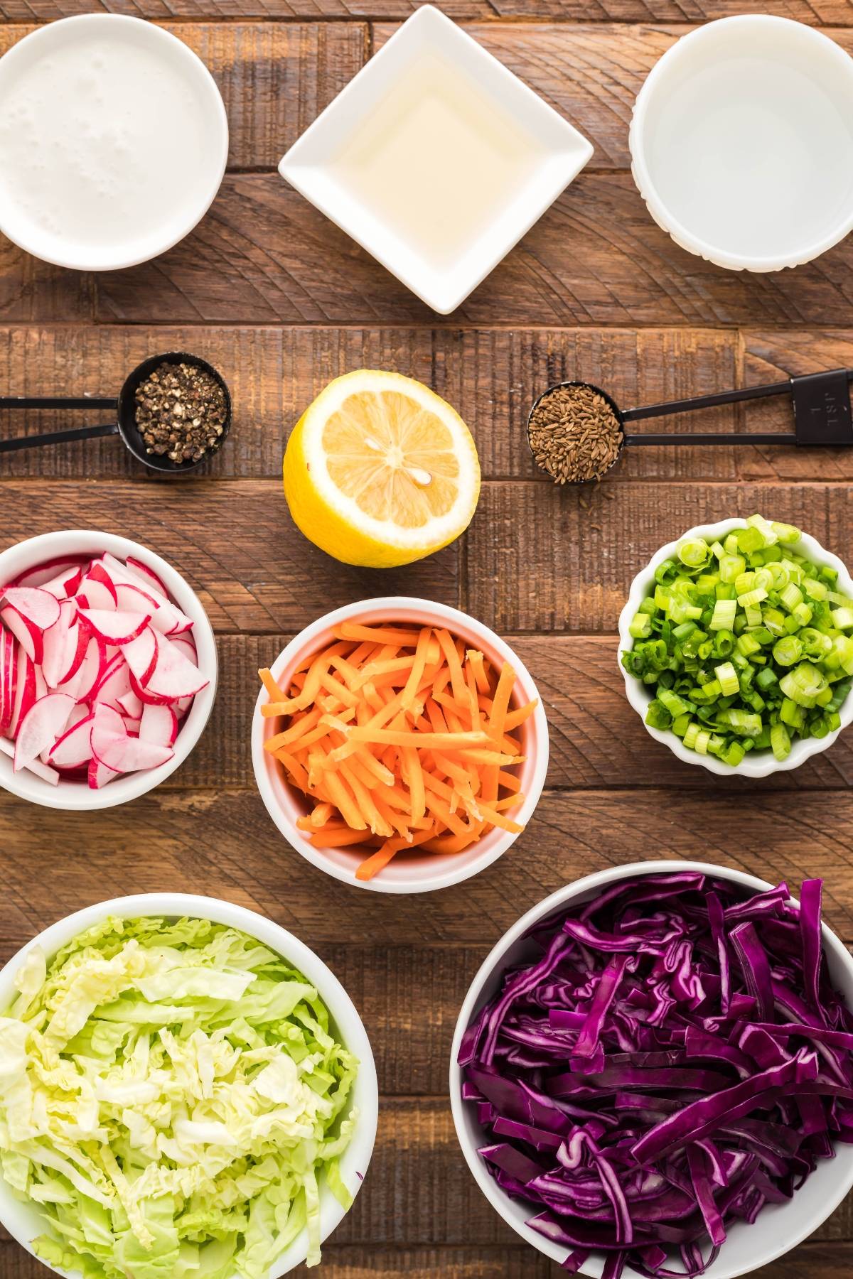 Bowls of sliced radish, carrots, lettuce, cabbage, green onions, spices, lemon, and small bowls of liquids make the perfect base for a Dairy Free Vegan Coleslaw to pair with pulled pork in a dutch oven.