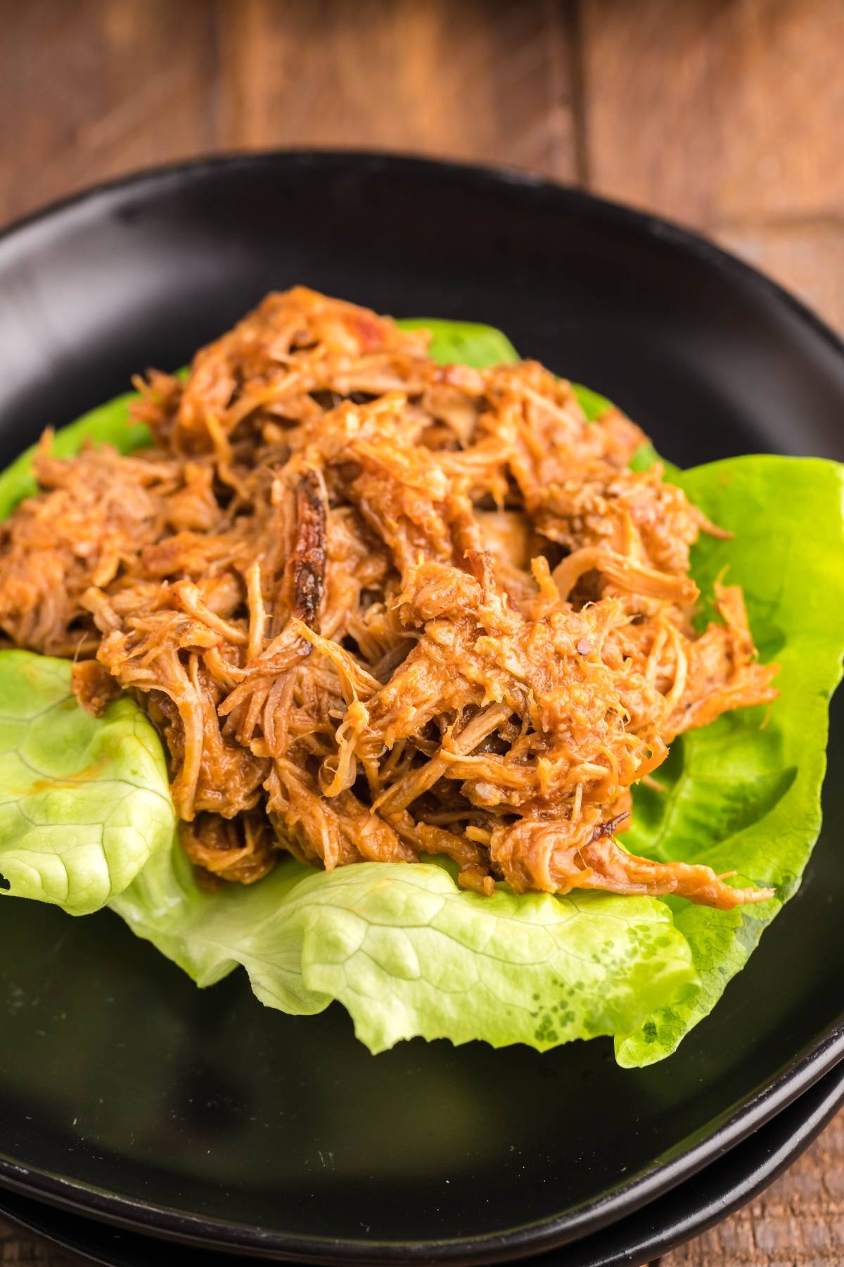 Pulled pork in lettuce wraps served on fresh green lettuce leaves, paired with a side of Pulled Pork and Dairy Free Coleslaw, all presented on a sleek black plate.