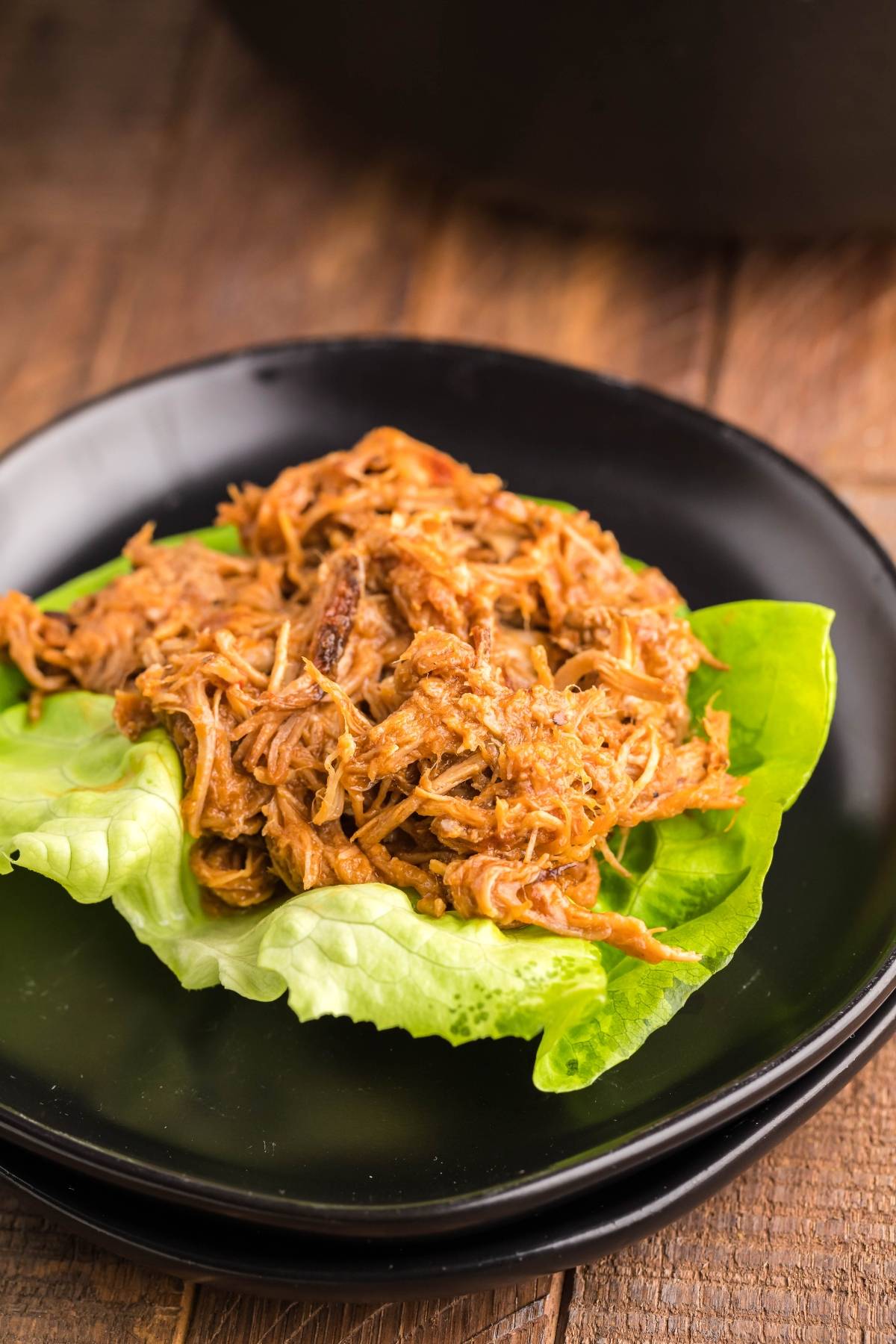 Slow cooked pork shoulder, shredded and served BBQ-style on a fresh green lettuce leaf, placed on a black plate.