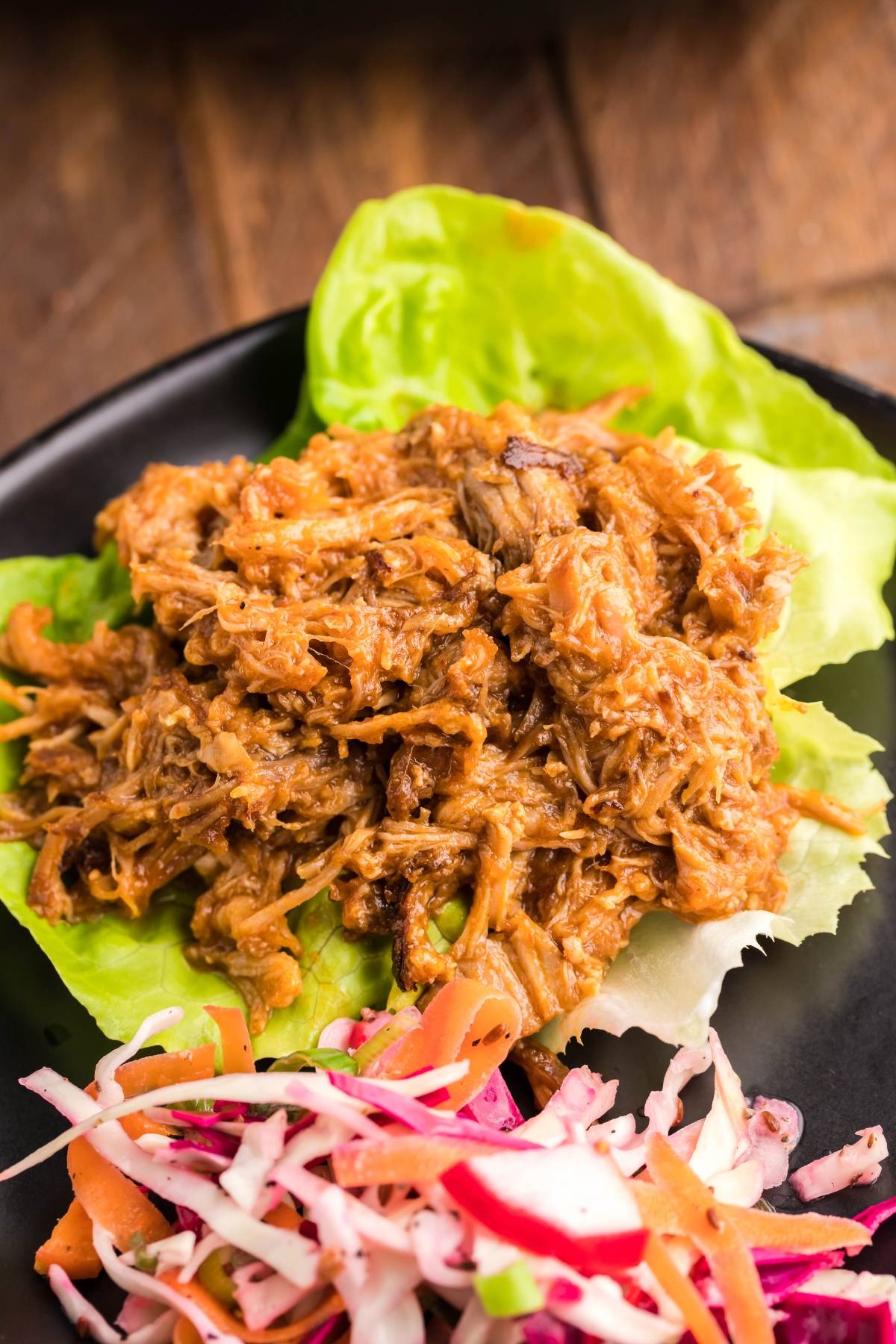 Slow cooked pork shoulder served on lettuce leaves with a side of Dairy Free Vegan Coleslaw, all presented on a sleek black plate.