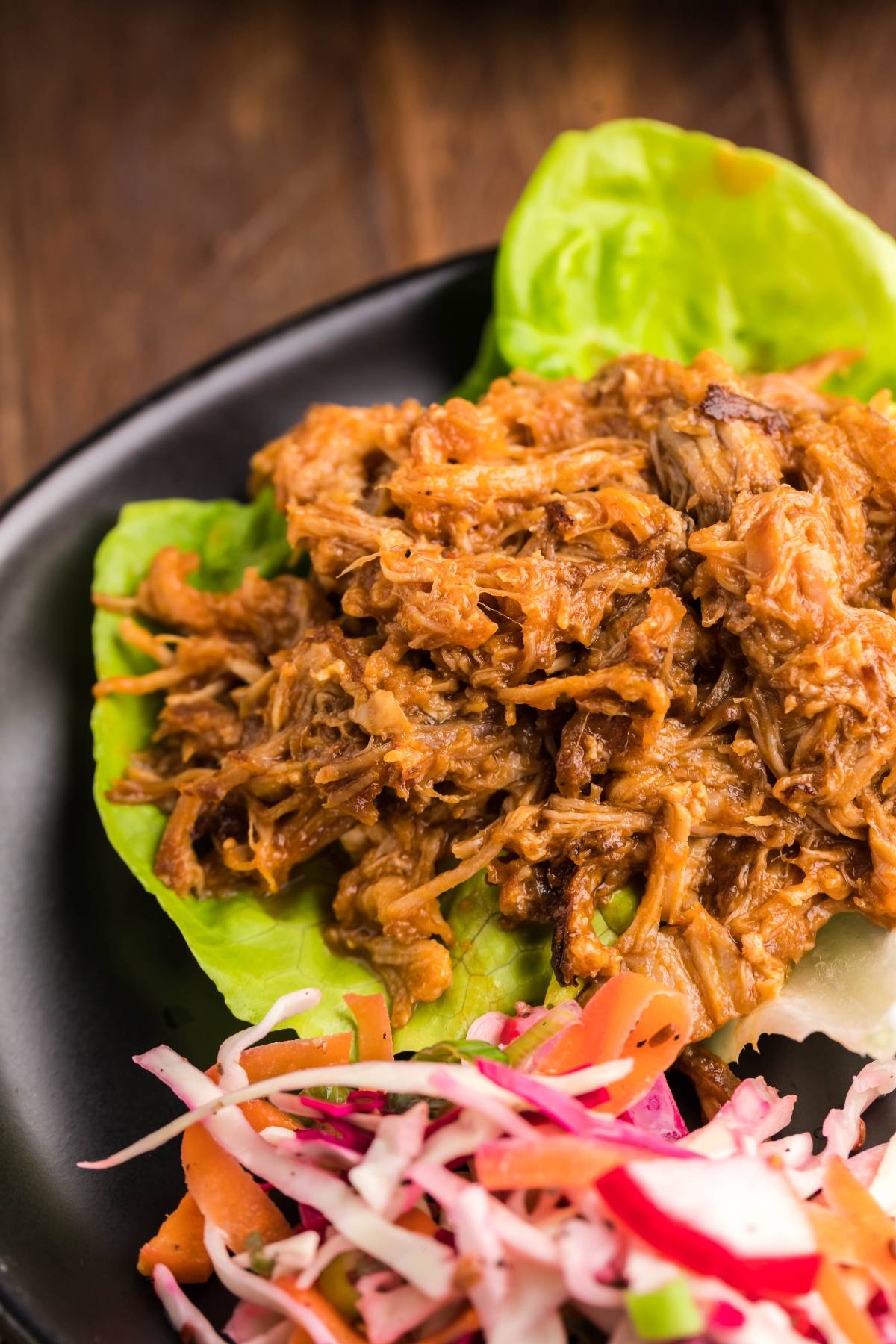 Slow cooked pork shoulder served on lettuce leaves with a side of colorful Dairy Free Vegan Coleslaw, all presented on a sleek black plate.