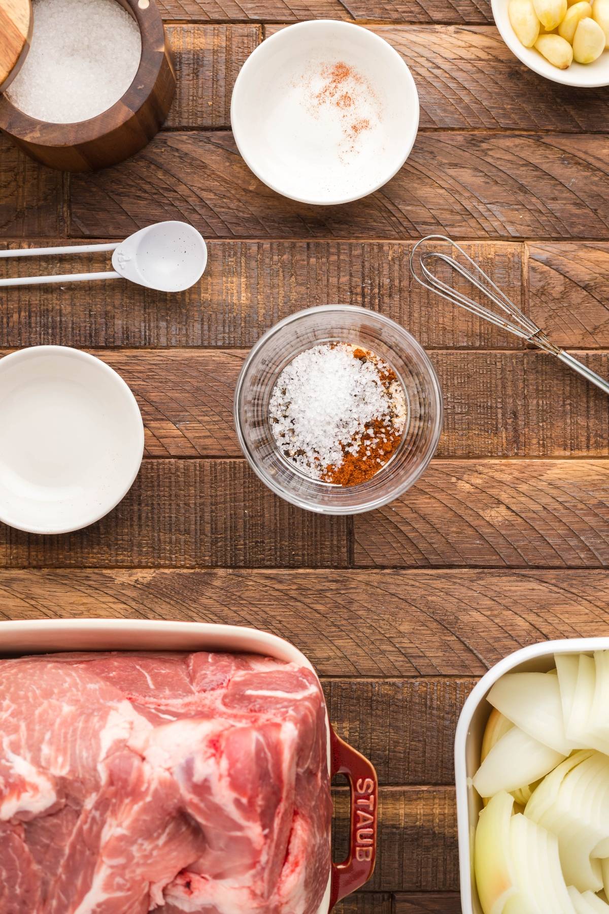 Overhead view of raw pork, sliced onions, spices, salt, and measuring spoons on a wooden surface—perfect for preparing slow cooked pork shoulder to pair with Dairy Free Vegan Coleslaw.