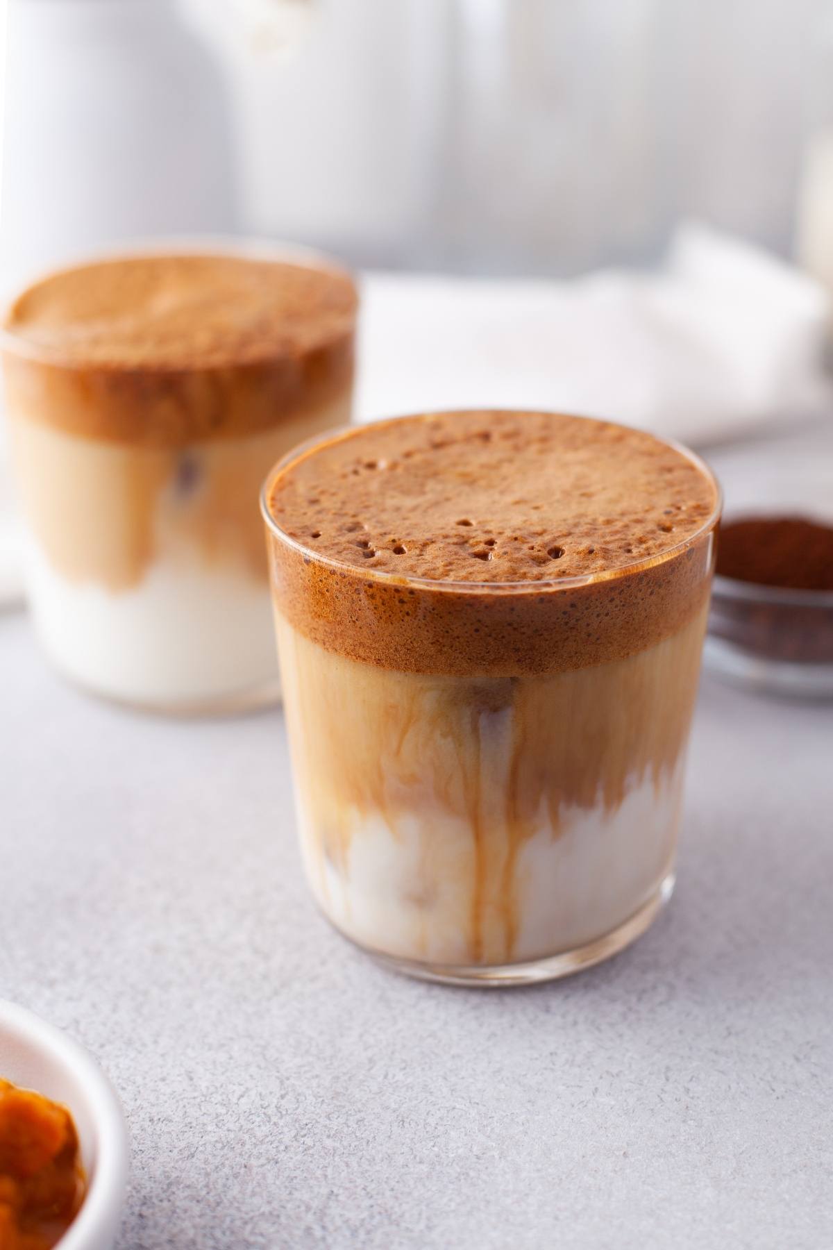 Two glasses of dalgona coffee with whipped coffee on top of iced milk, offering an autumn coffee flavour perfect as a seasonal coffee recipe.