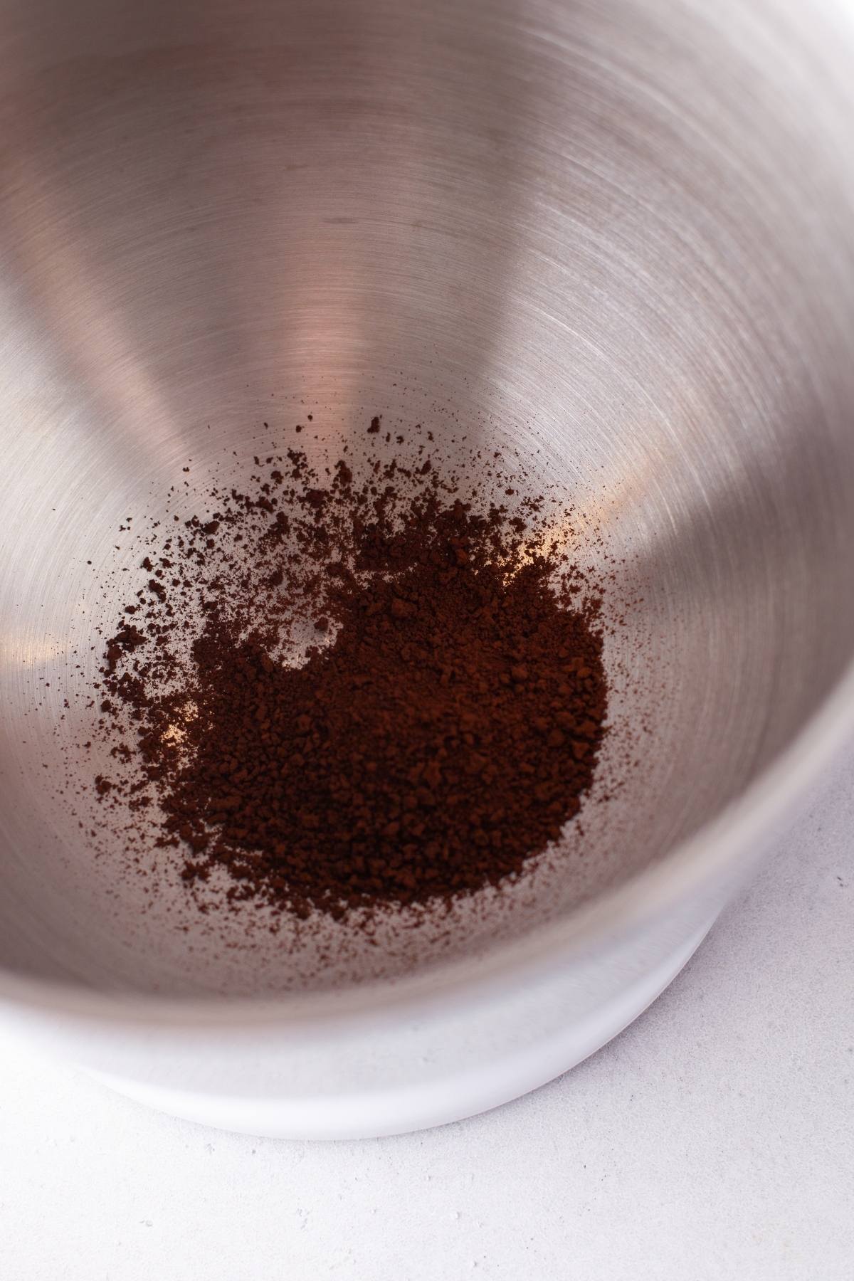 Ground coffee in the bottom of a large, empty stainless steel mixing bowl, ready to be transformed into a delicious pumpkin whipped coffee with that cozy autumn coffee flavour.