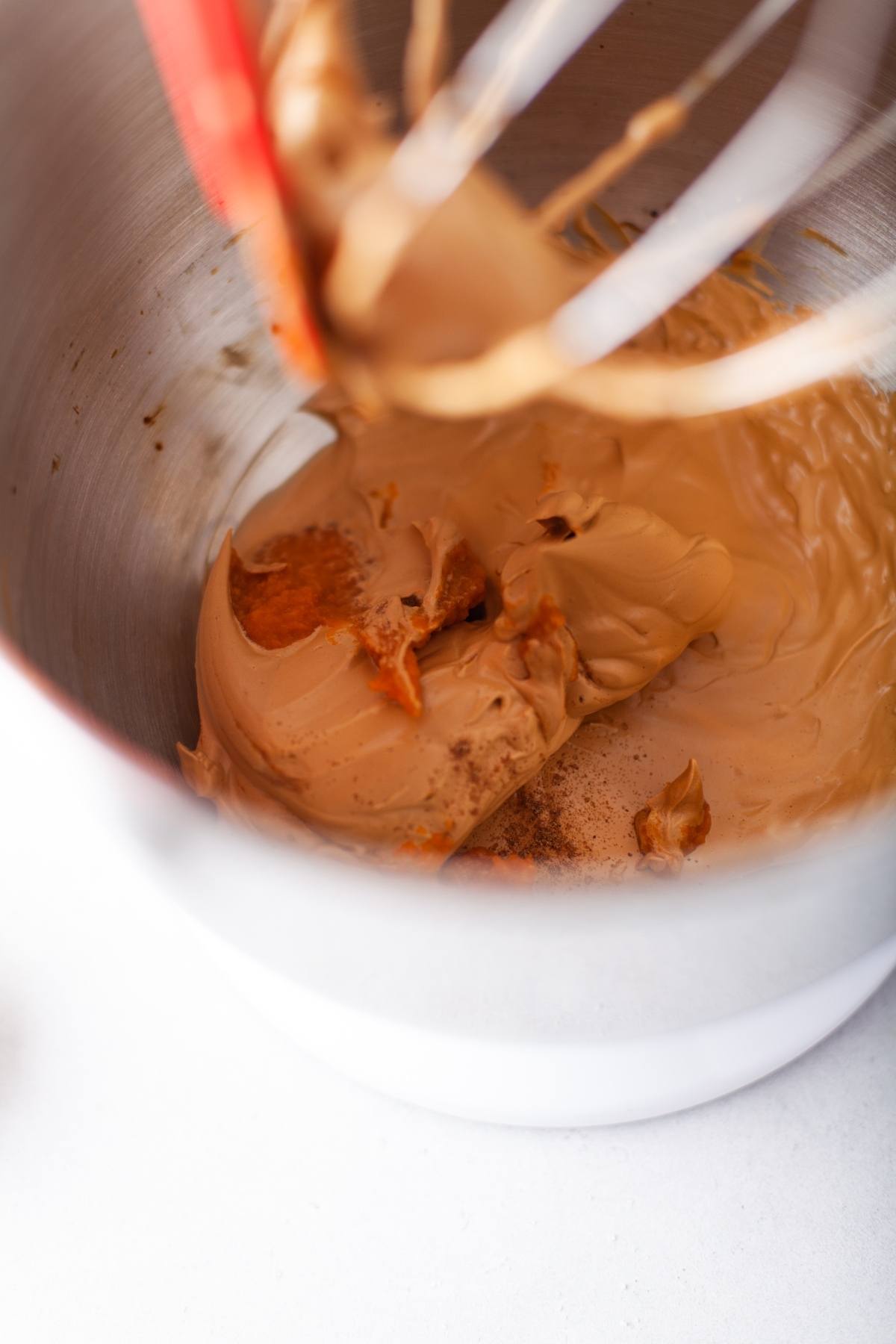 Close-up of peanut butter and pumpkin puree being mixed in a metal stand mixer bowl with a whisk attachment, perfect for adding an autumn coffee flavour to your treats.