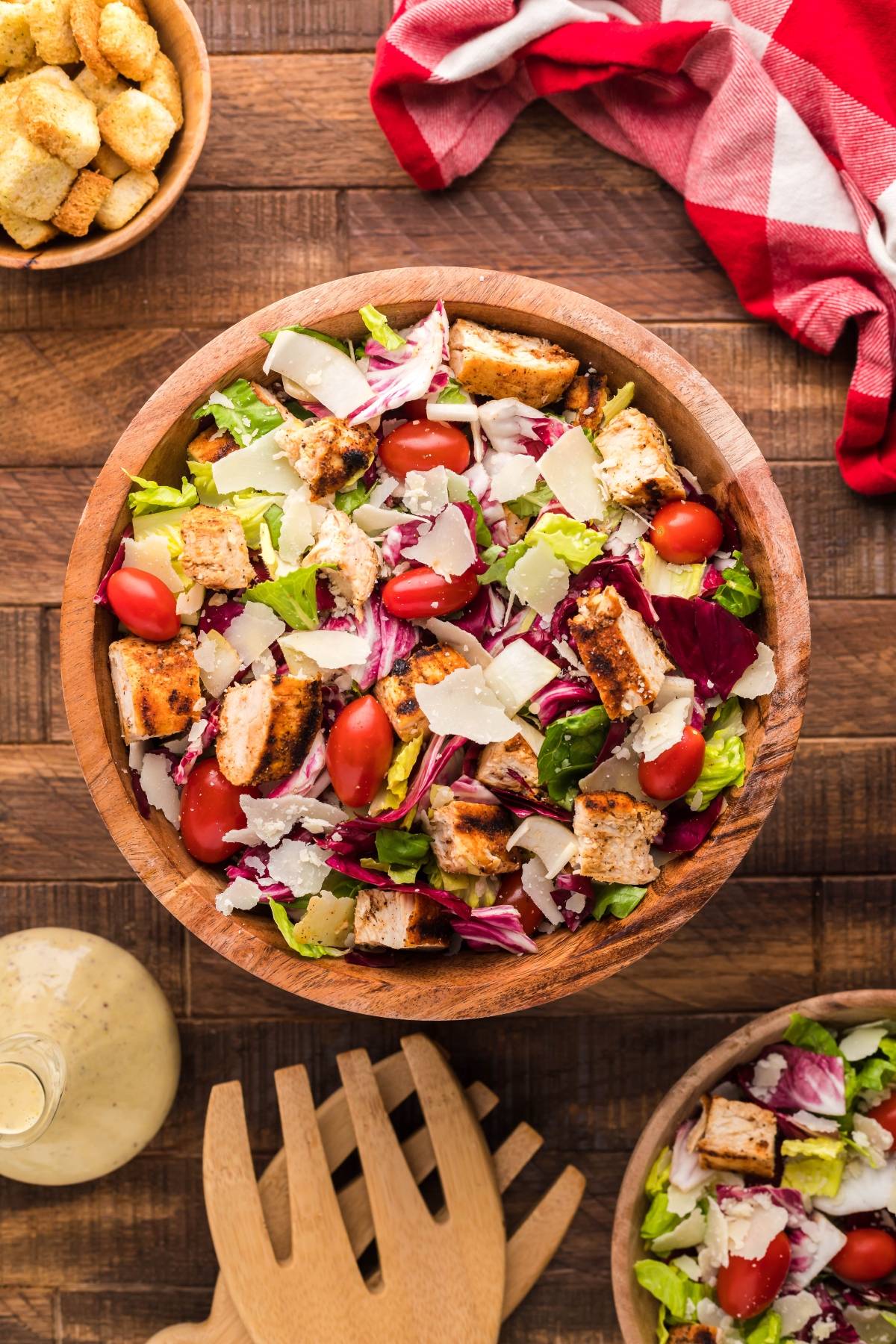 Wooden bowl of summer BBQ chicken salad Caesar-style with cherry tomatoes, lettuce, shaved parmesan, and a hint of radicchio and endive on a wooden table.