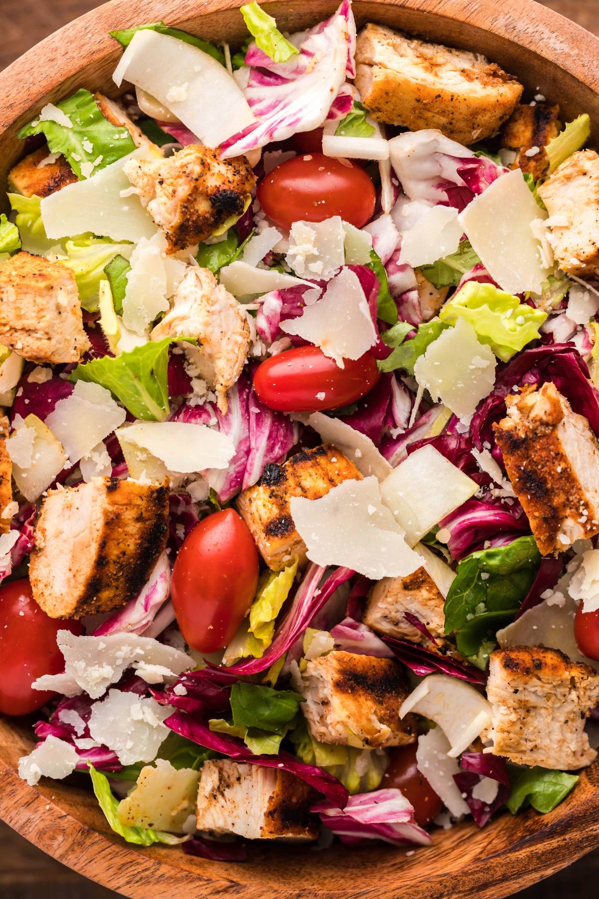 A salad made with radicchio and endive, grilled chicken, cherry tomatoes, mixed greens, and shaved parmesan, all tossed together in a wooden bowl. Perfectly paired with a creamy honey mustard dressing.