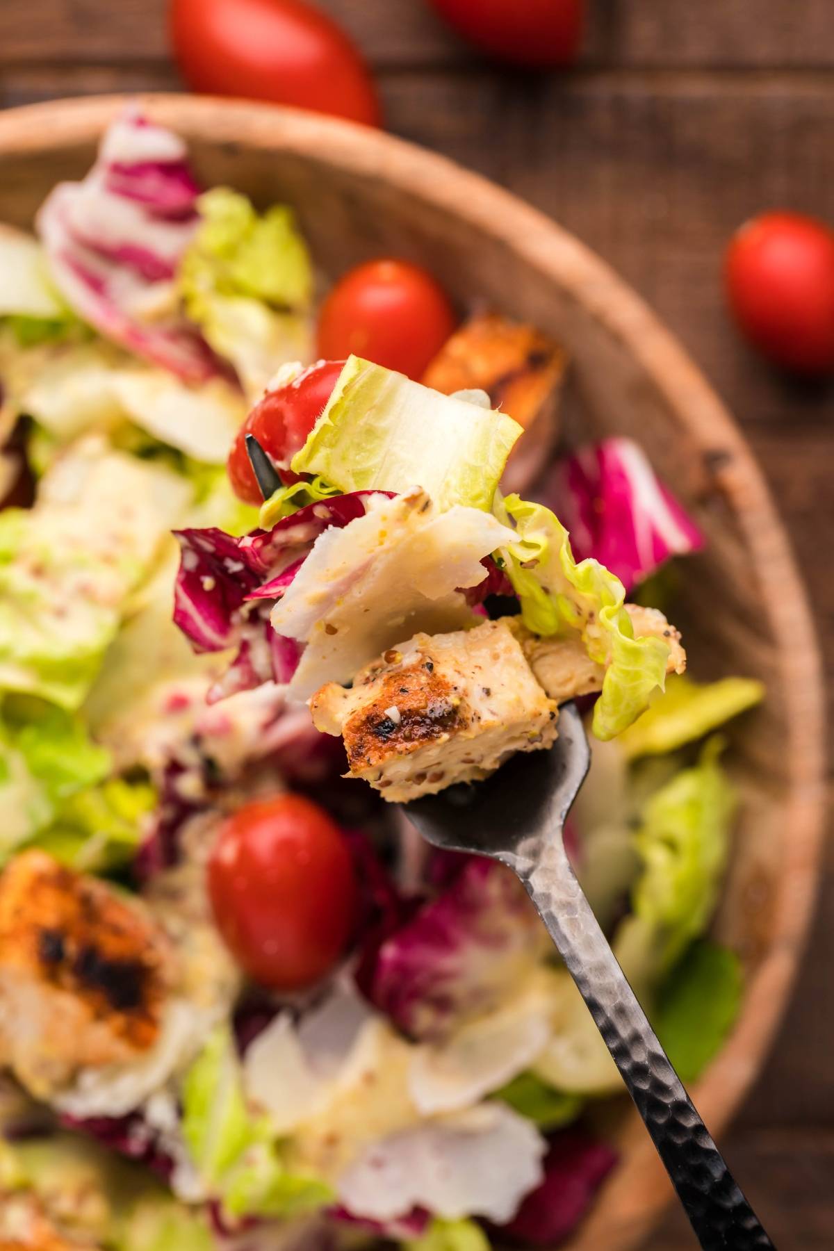 A close-up of a forkful of salad with grilled chicken, lettuce, tomatoes, and shredded cheese in a wooden bowl, topped with creamy honey mustard dressing.