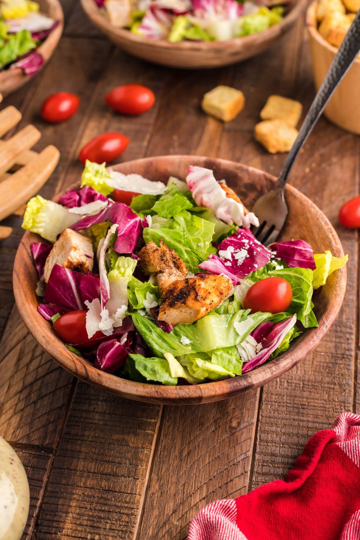 A wooden bowl of summer BBQ chicken salad with grilled chicken, lettuce, tomatoes, and parmesan cheese sits on a rustic table, perfect with Creamy Honey Mustard Dressing.