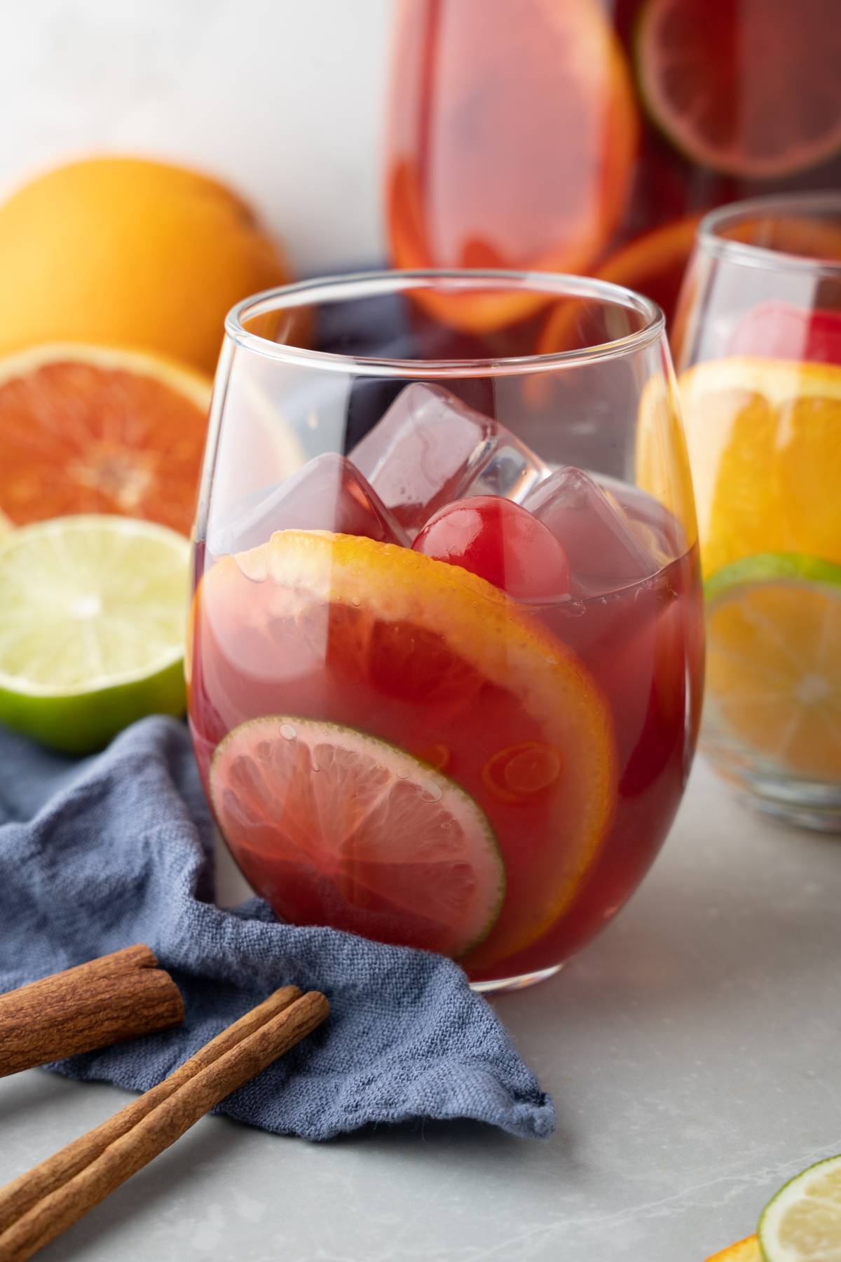 A glass of Pinot noir fruit sangria with ice, orange, lime slices, and cinnamon sticks sits on the table.