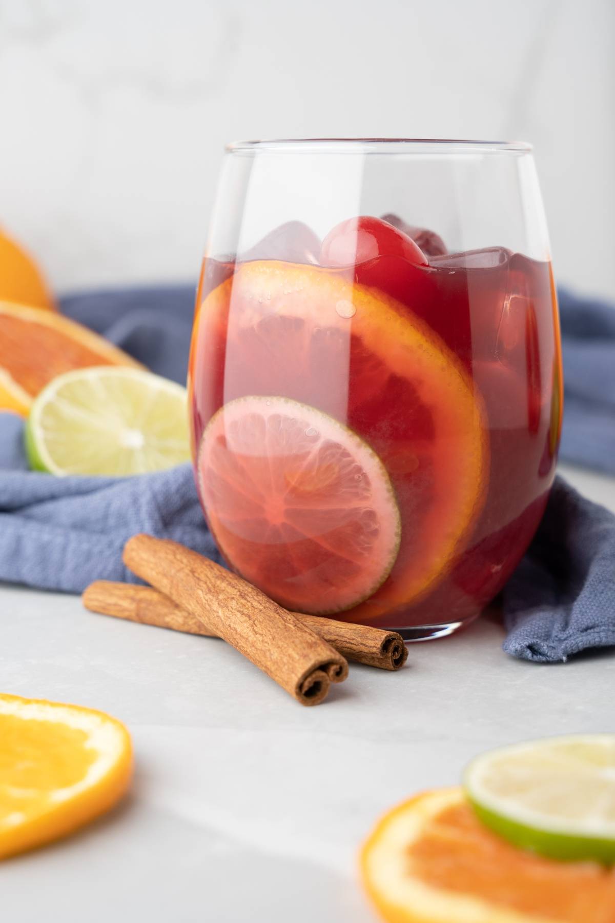 A glass of rum punch sangria with orange, lime slices, and cinnamon sticks sits on the table.