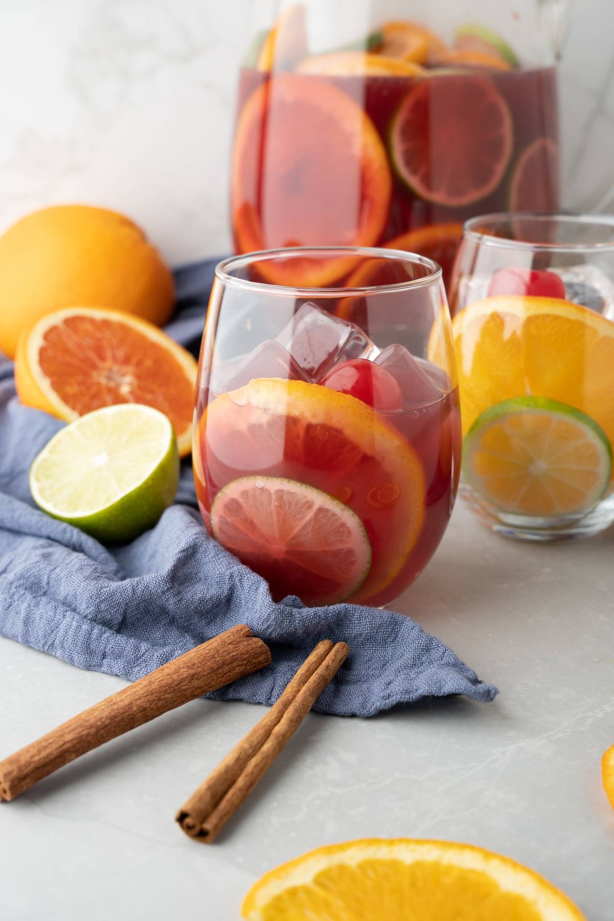 A glass of sangria with ice, orange, and lemon slices, plus cinnamon sticks and fresh fruit nearby—perfect for a refreshing Pinot noir fruit sangria.