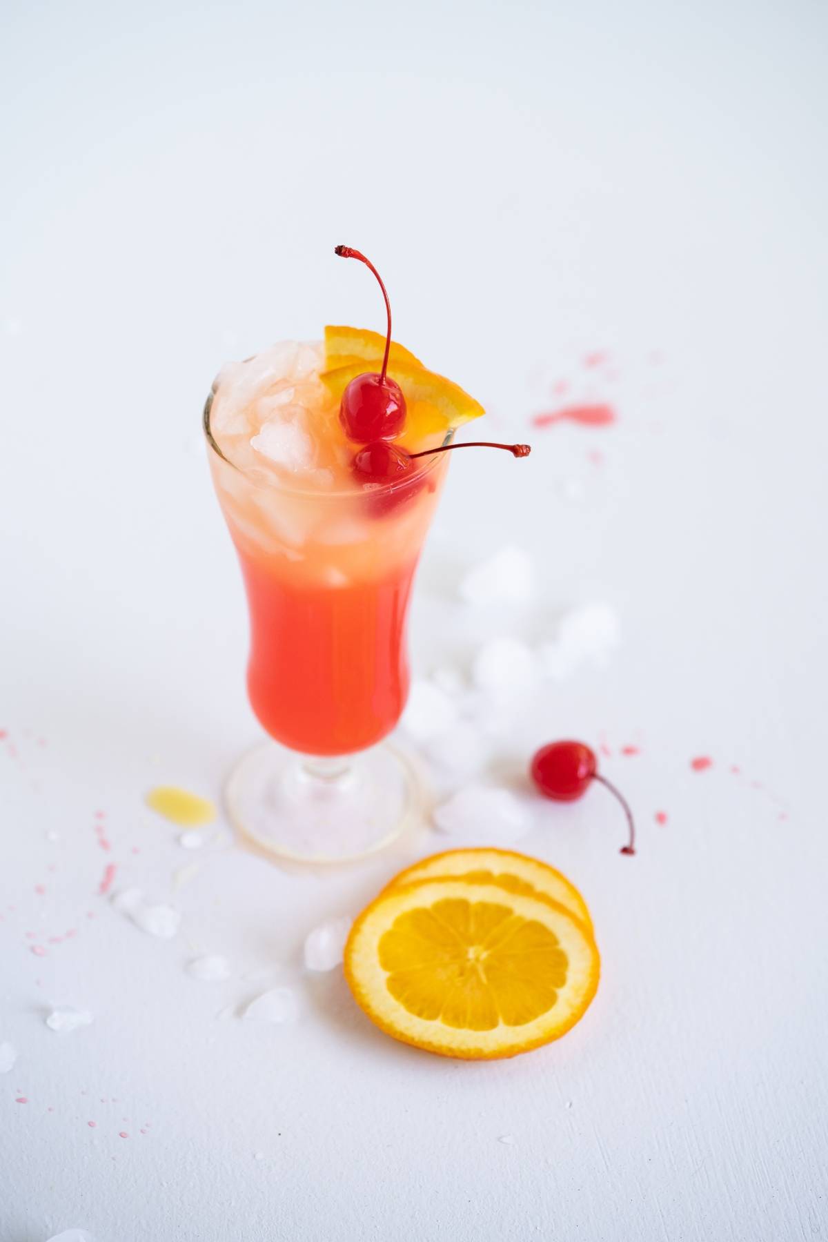 A tropical cocktail with ice, cherry, and orange slice garnish beside orange slices and a cherry on the table—this easy rum runner recipe is perfect for anyone wanting to learn how to make a rum runner at home.