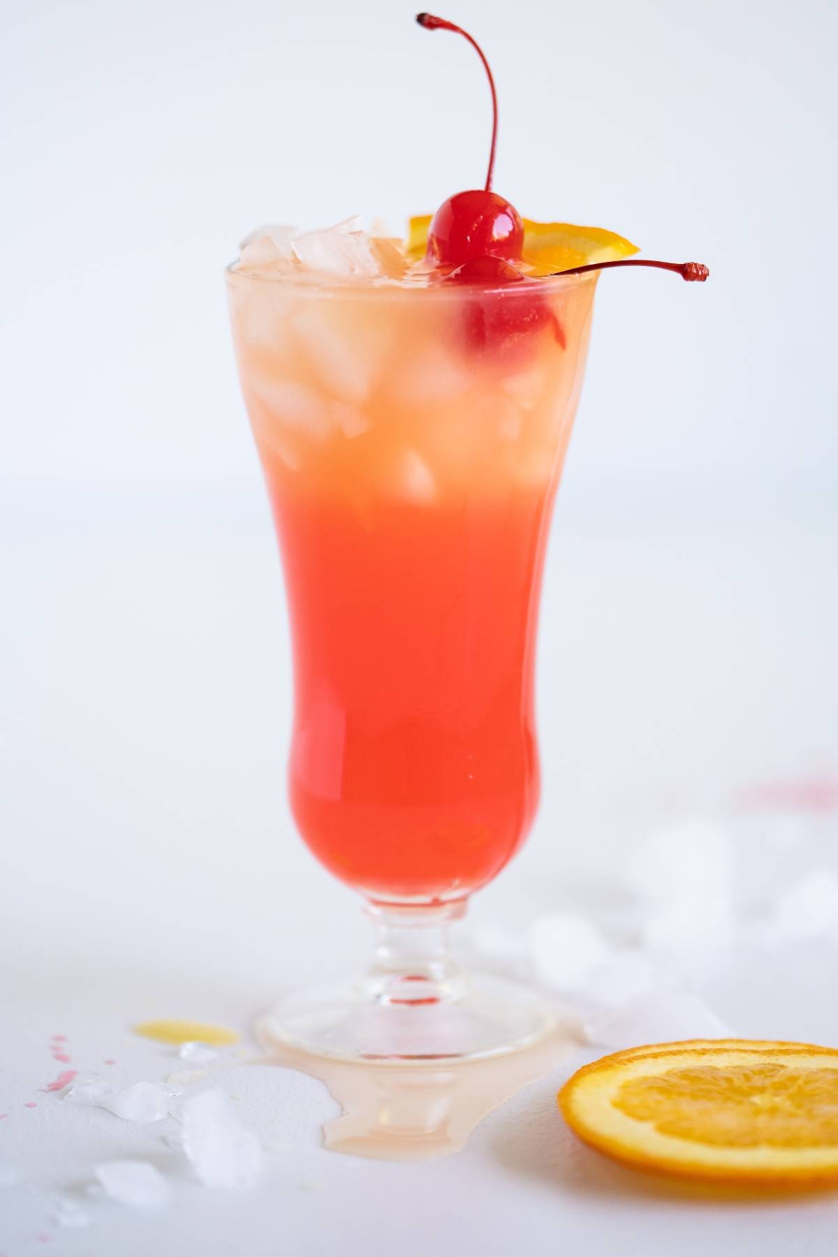 A bright orange-red rum runner cocktail with ice, garnished with a cherry and orange slice in a tall glass—perfect if you're searching for an easy rum runner recipe.