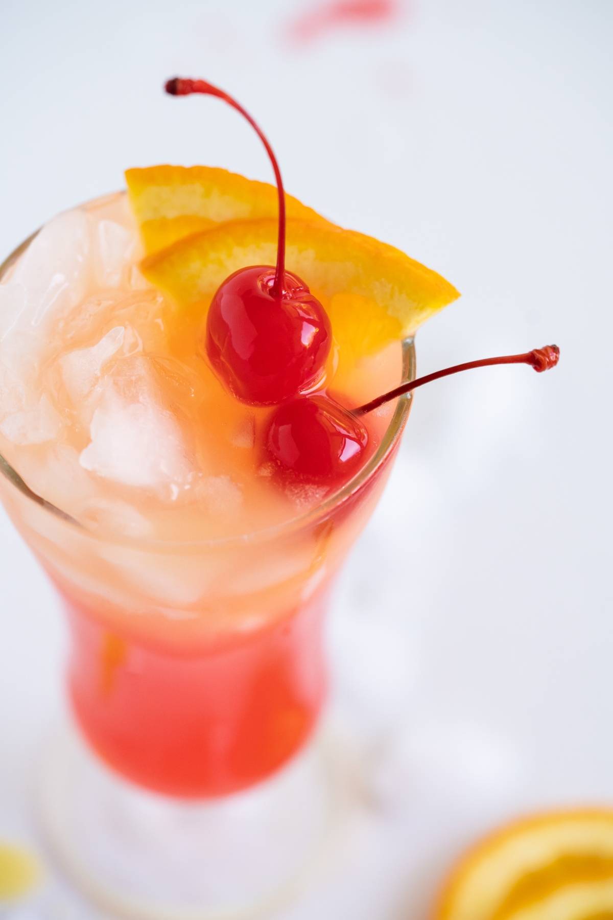 A tropical cocktail with ice, two cherries, and an orange slice garnish in a tall glass, perfect for fans of a classic rum runner cocktail.