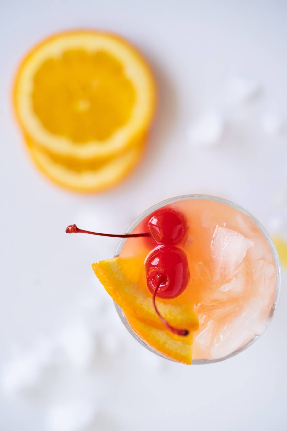 A Caribbean punch cocktail recipe with ice, an orange slice, and two cherries, featuring vibrant orange slices in the background.