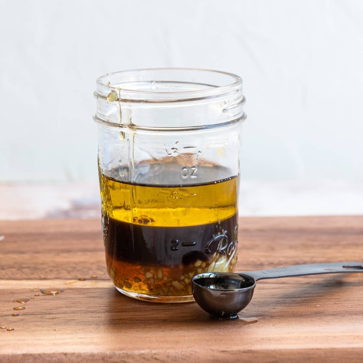 A glass jar with honey ginger dressing, perfect for a cabbage salad recipe, sits beside a black measuring spoon on a wooden surface.
