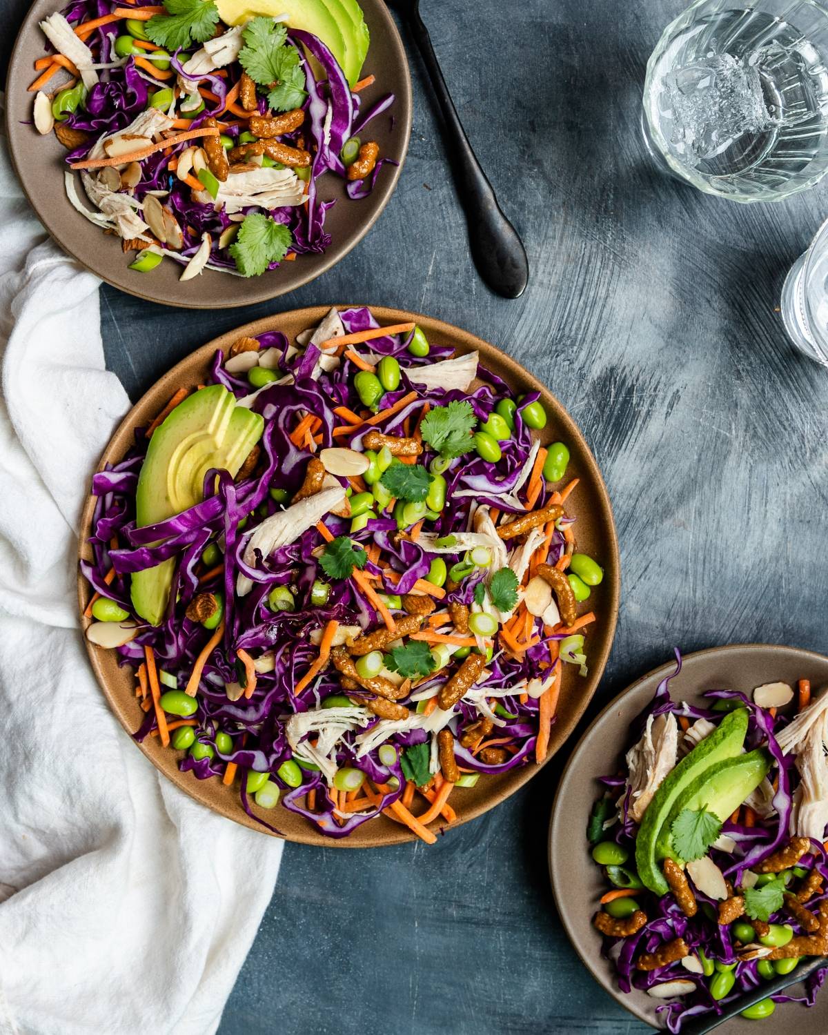 Three plates of colorful salad with shredded chicken, red cabbage, carrots, edamame, avocado, and cilantro—an irresistible cabbage salad recipe perfect with a drizzle of honey ginger dressing.