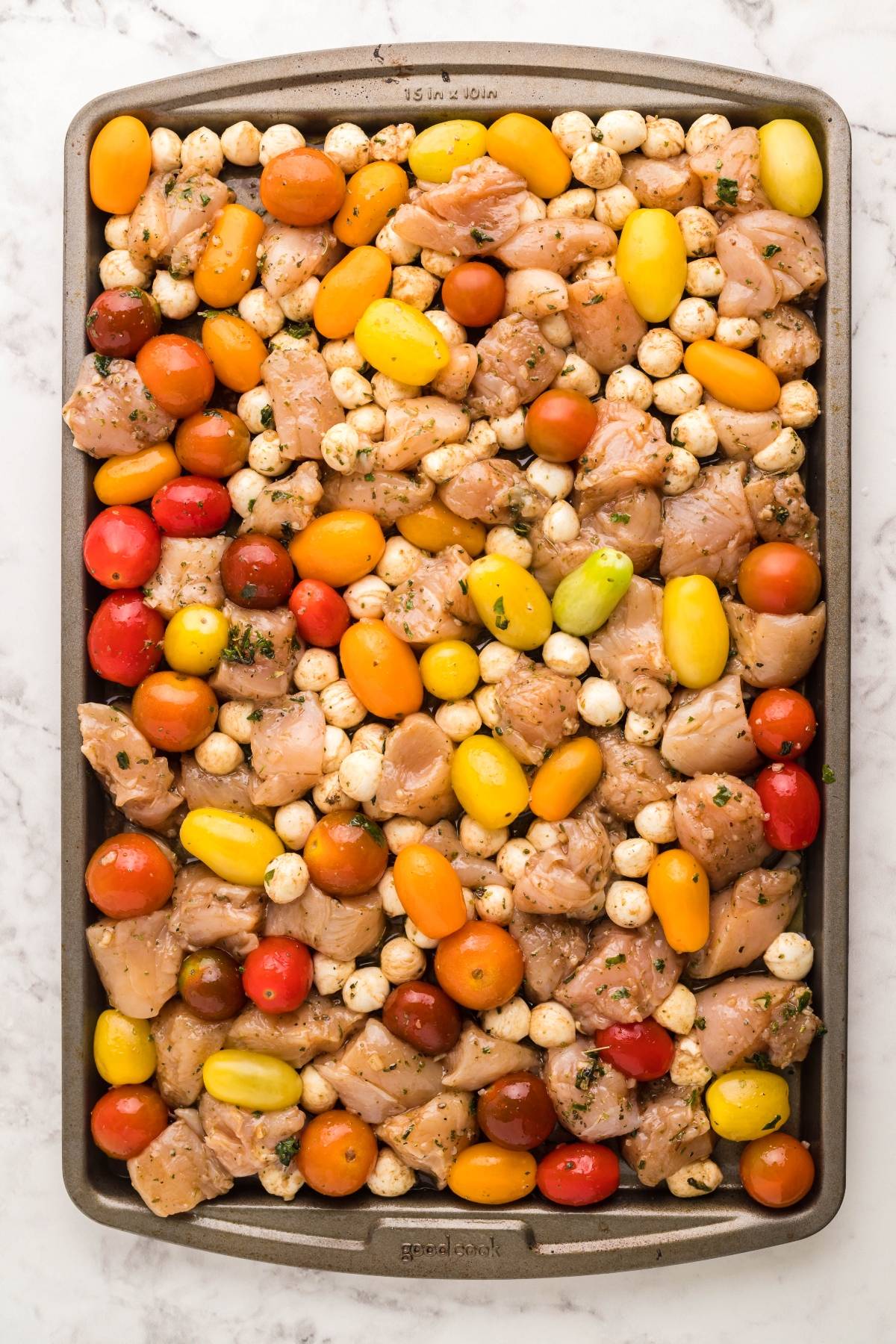 Raw chicken pieces, colorful cherry tomatoes, and mozzarella balls arranged on a baking sheet for an easy oven chicken caprese—a perfect easy chicken dinner.