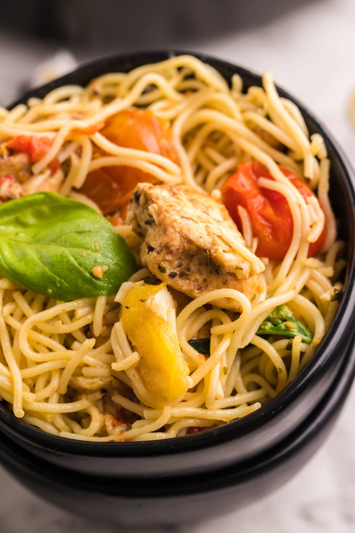 Spaghetti with grilled chicken tenderloins, cherry tomatoes, and basil served in a black bowl.