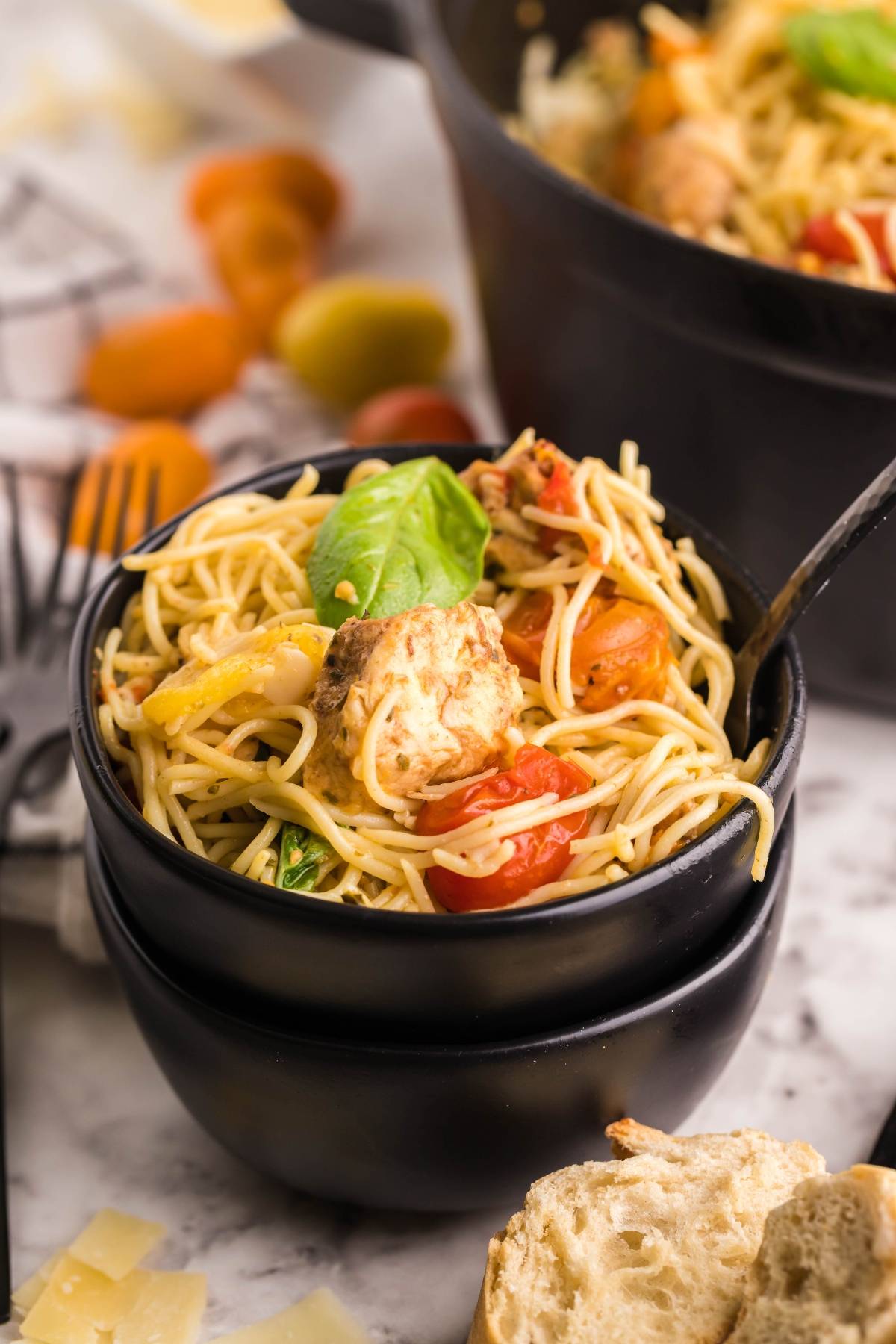 Bowl of spaghetti with cherry tomatoes, basil, and chunks of cheese, inspired by baked chicken caprese with pasta, served with bread and parmesan on the side.