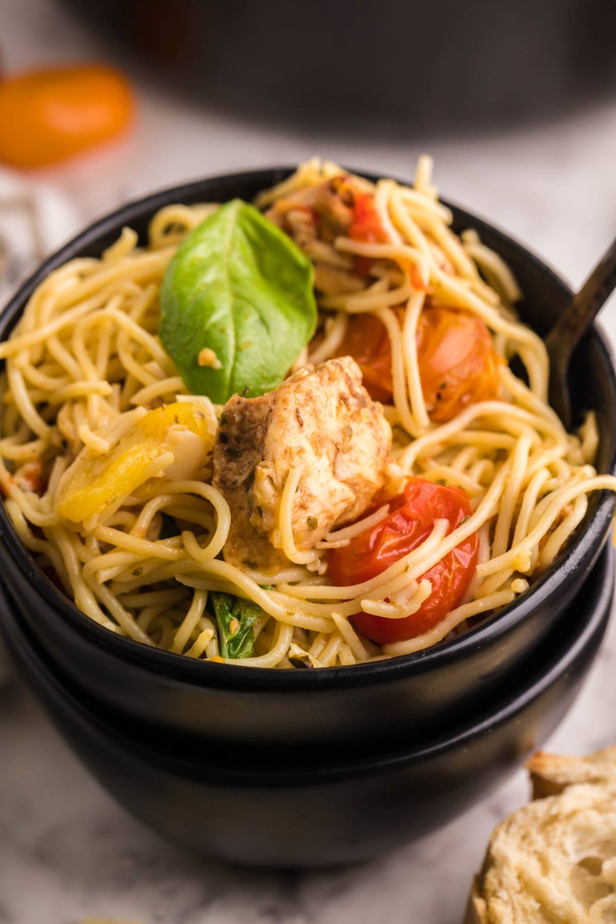 Bowl of spaghetti with chicken tenderloins, cherry tomatoes, basil, and yellow peppers, served with a fork—an easy chicken dinner inspired by Sheet Pan Chicken Caprese Pasta.