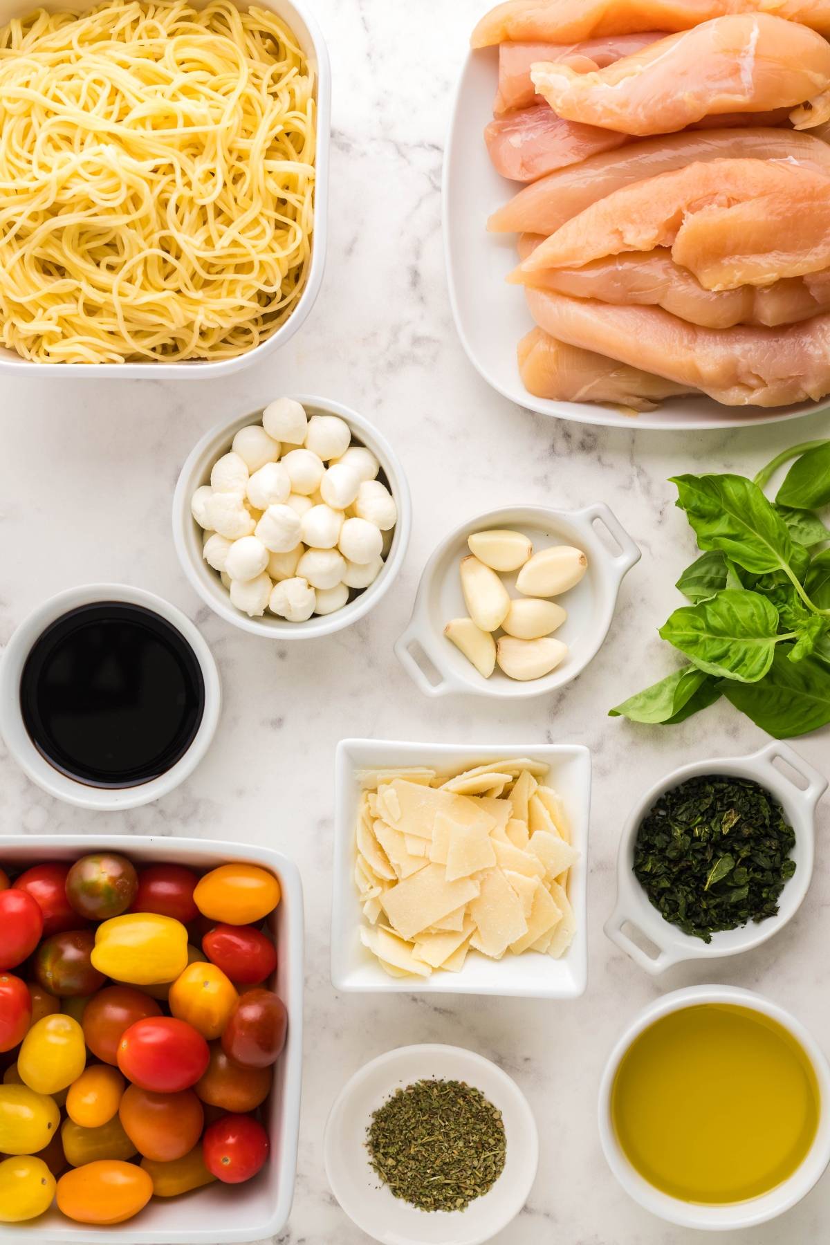 Ingredients for an easy chicken dinner: Sheet Pan Chicken Caprese Pasta made with chicken tenderloins, pasta, tomatoes, mozzarella, basil, garlic, oil, vinegar, and cheese.