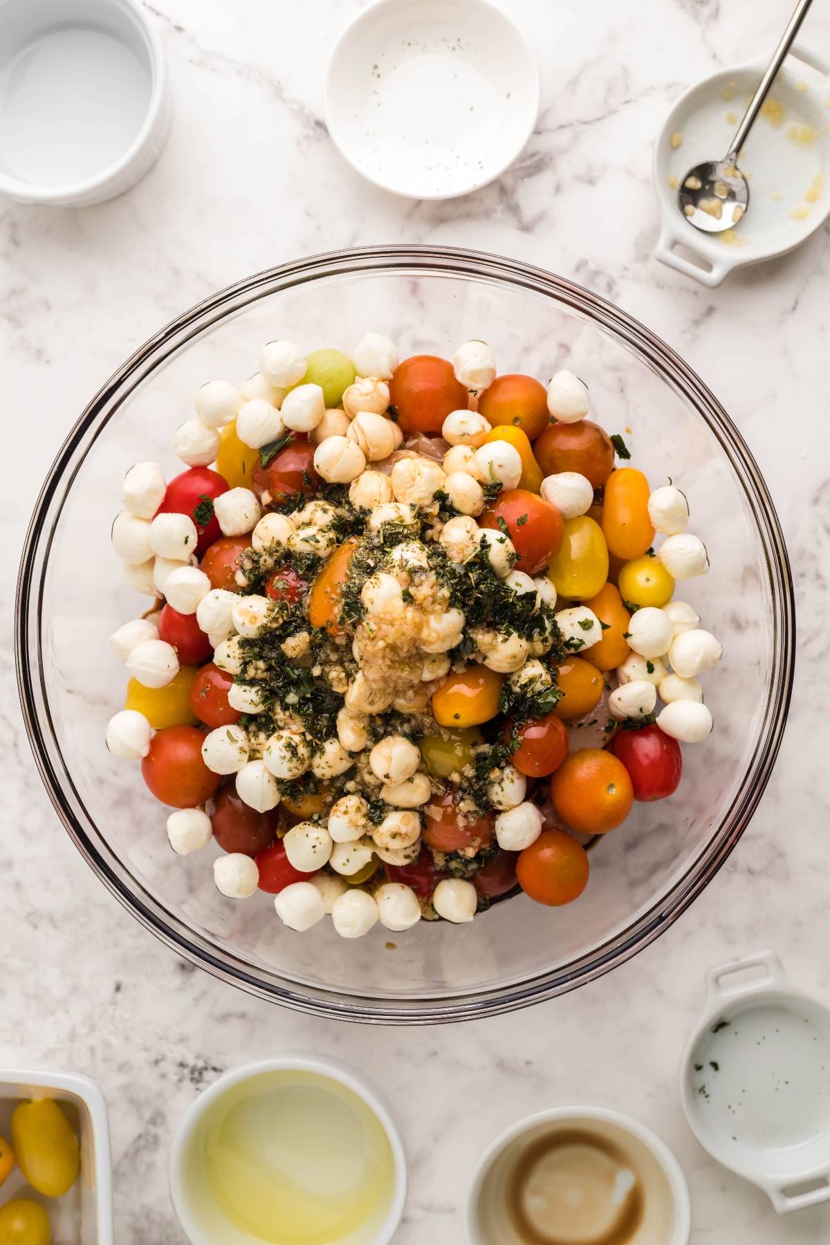 A glass bowl with cherry tomatoes, mozzarella balls, chickpeas, and herbs on a marble countertop—perfect as a fresh side for easy oven chicken caprese or your favorite baked chicken caprese with pasta.