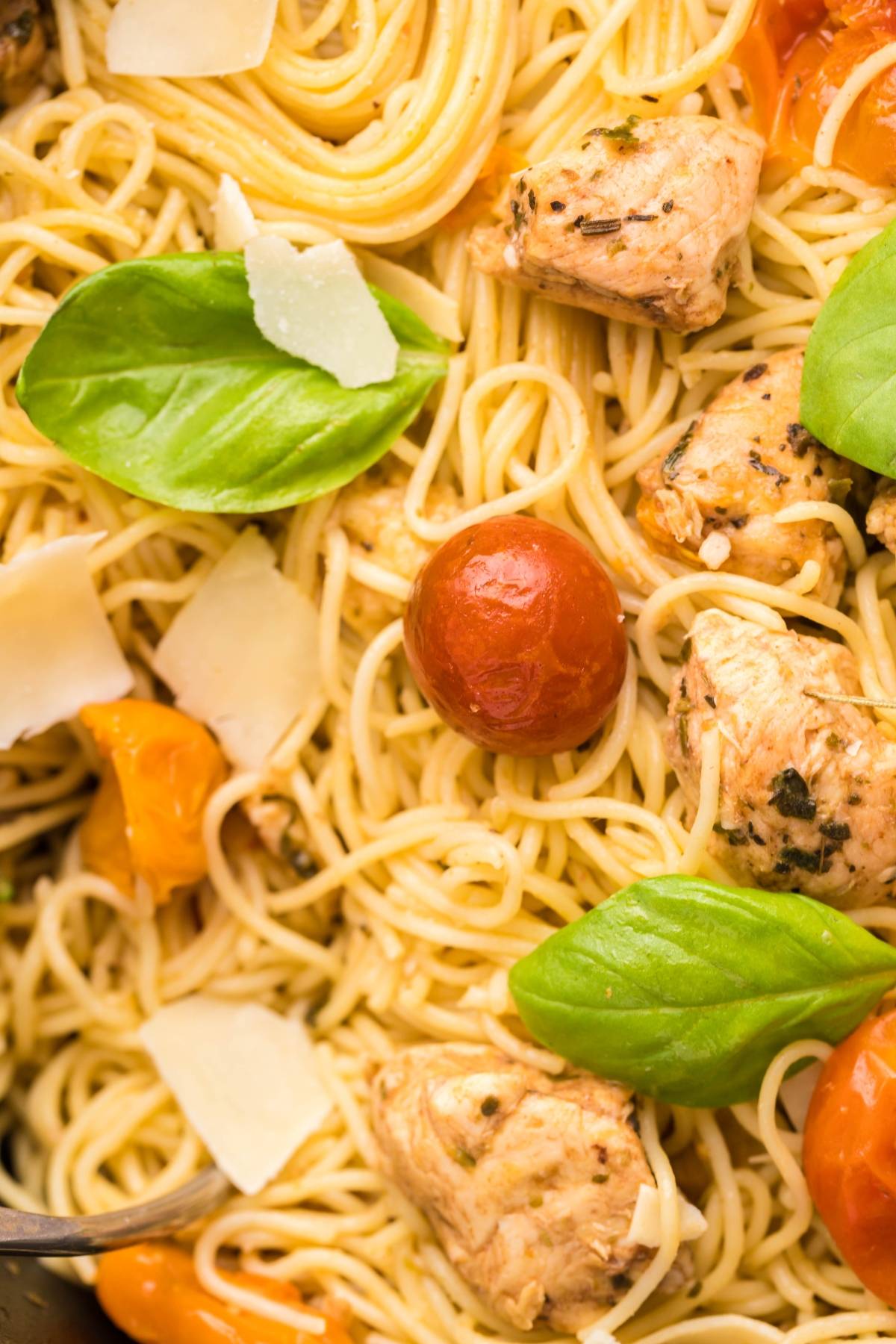 Close-up of Sheet Pan Chicken Caprese Pasta featuring spaghetti, tender chicken pieces, cherry tomatoes, basil leaves, and parmesan shavings—an easy chicken dinner bursting with fresh flavors.