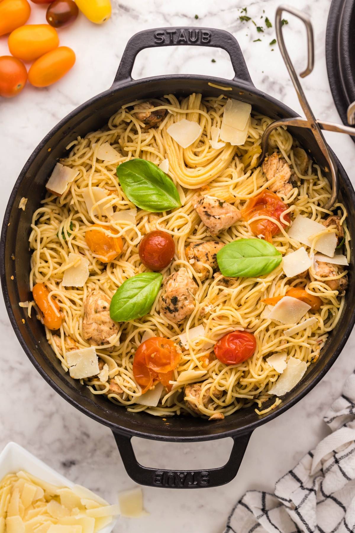 Spaghetti with chicken tenderloins, cherry tomatoes, basil, and parmesan in a black pot on a marble countertop—an easy chicken dinner packed with fresh flavors.