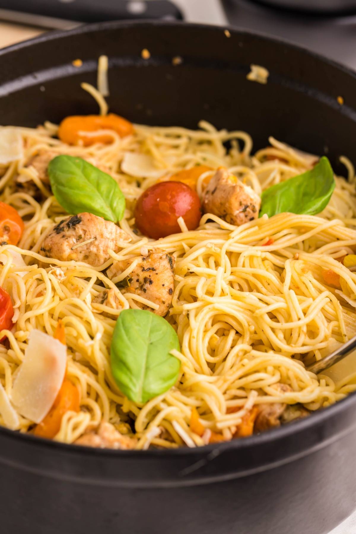 Spaghetti with chicken tenderloins, cherry tomatoes, basil leaves, and parmesan in a black pan—an easy oven chicken caprese perfect for a quick and delicious dinner.