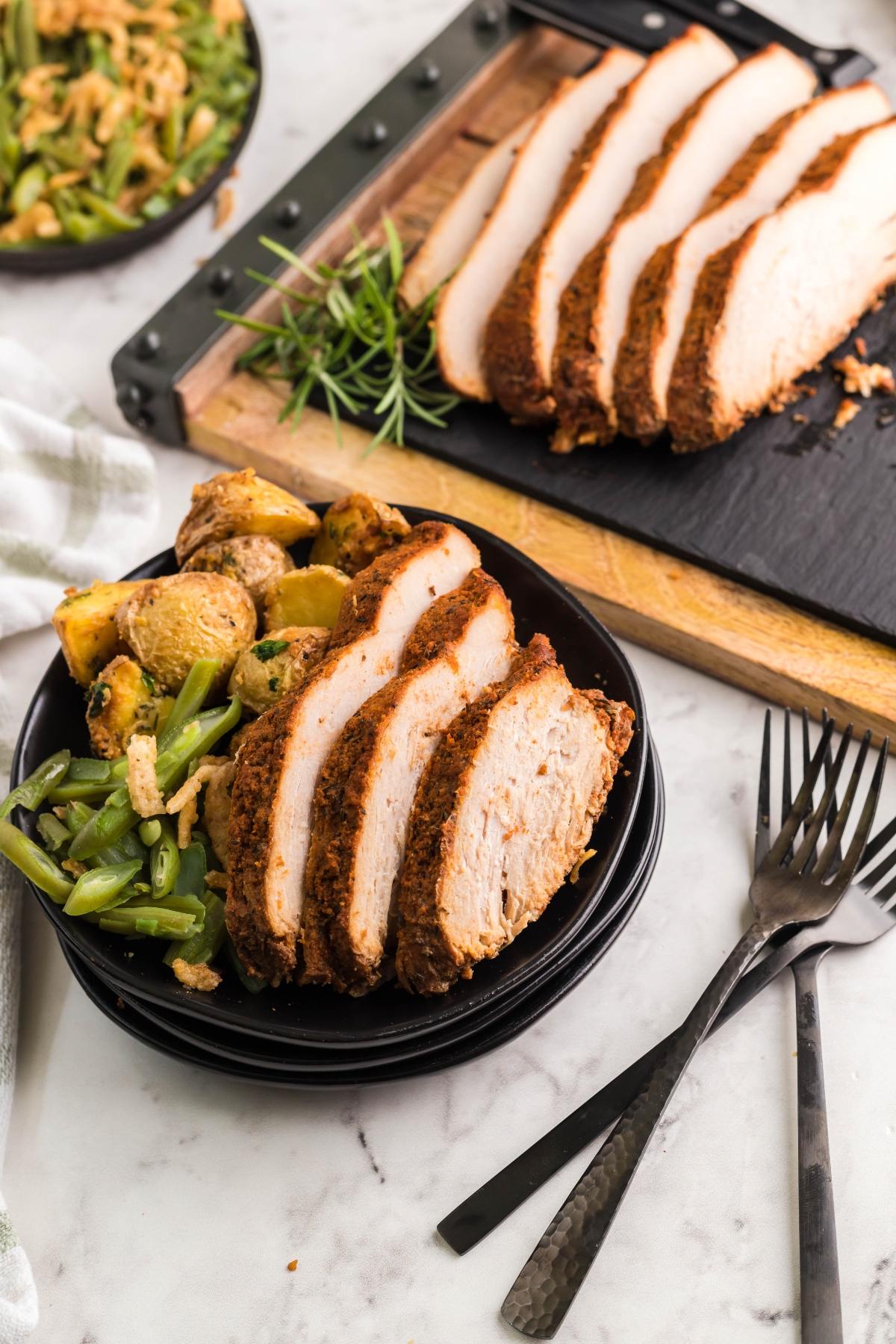 Sliced seasoned turkey breast—prepared using an easy brine for turkey breast—served with green beans and roasted potatoes on a plate, utensils beside it.
