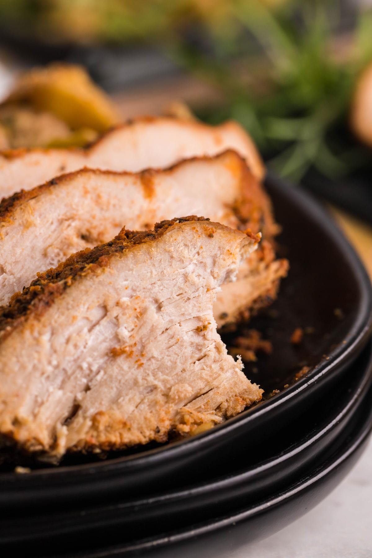 Close-up of sliced, seasoned baked pork on a black plate, showing a juicy and tender texture—similar to the results you get with boneless turkey breast in a slow cooker.