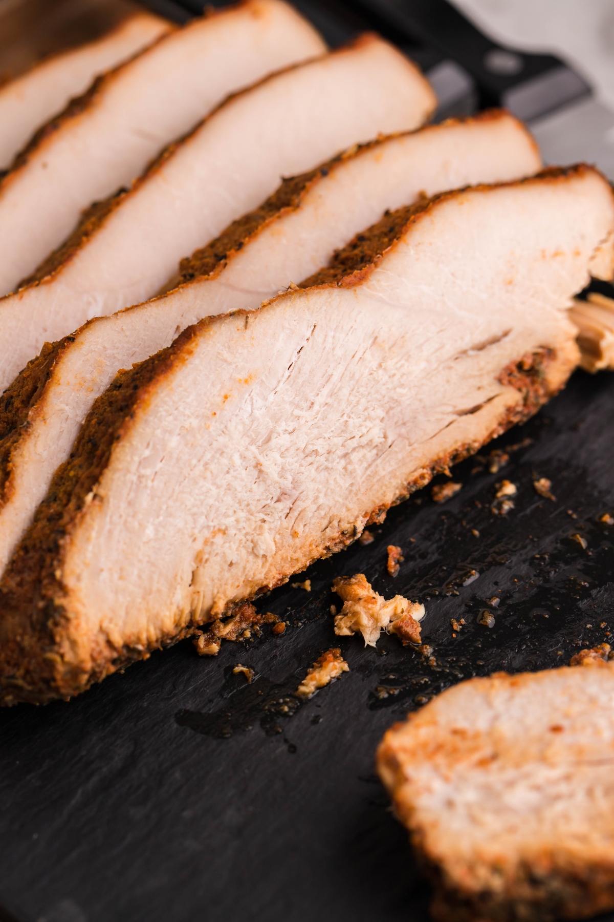 Sliced cooked turkey breast on a dark cutting board, showing a juicy and seasoned interior—perfect results from our boneless turkey breast in a slow cooker.