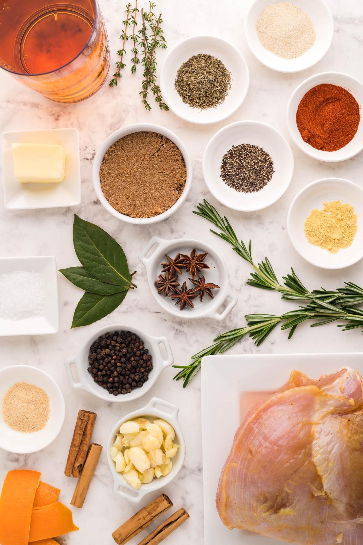 Assorted spices, herbs, butter, garlic, and raw turkey on a marble surface, arranged neatly in small dishes—perfect for prepping an easy brine for turkey breast or creating a flavorful boneless turkey breast in a slow cooker.