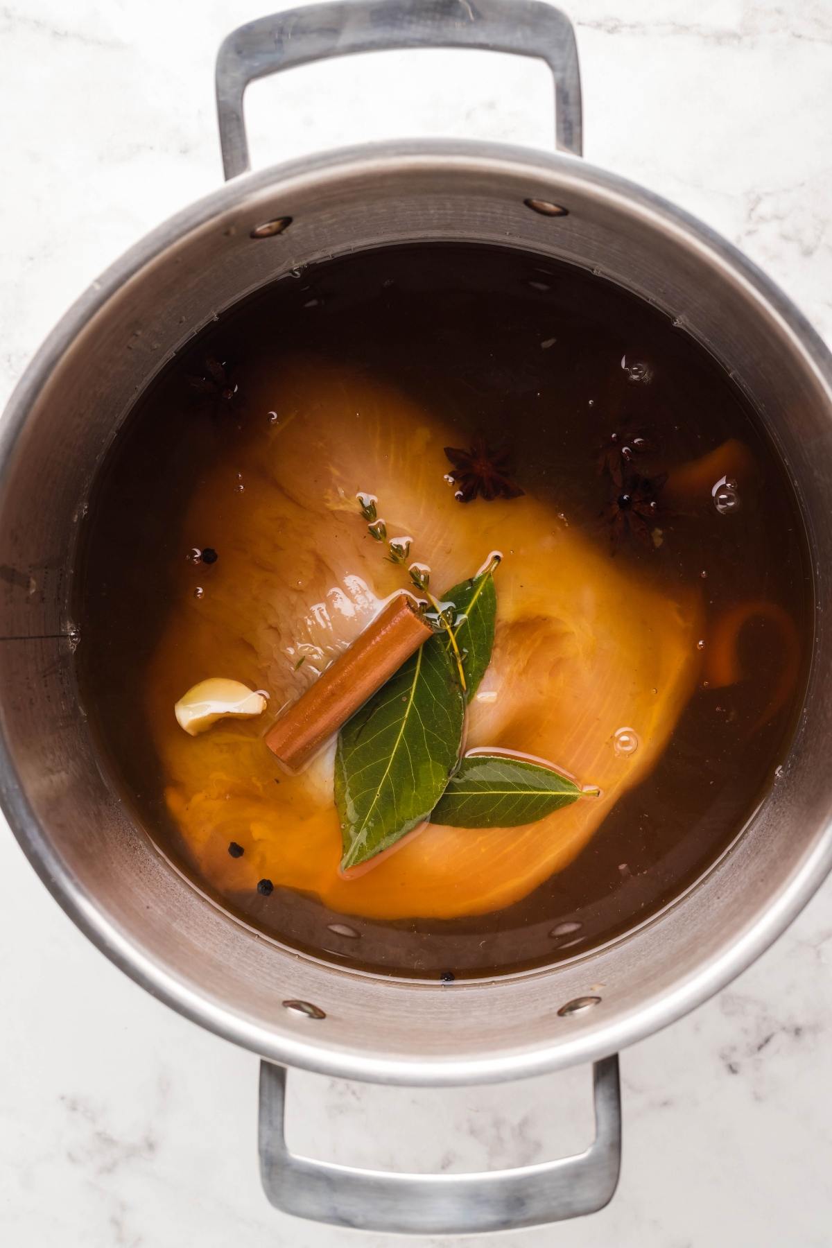 Large pot filled with liquid, chicken breasts, bay leaves, cinnamon stick, garlic, and spices—similar to the comforting flavors in a slow cooker turkey breast recipe.