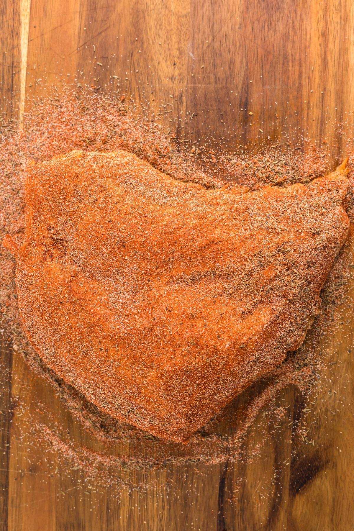 A large piece of meat covered in dry spice rub on a wooden cutting board, perfect for an easy brine for turkey breast or as the first step in your favorite slow cooker turkey breast recipe.