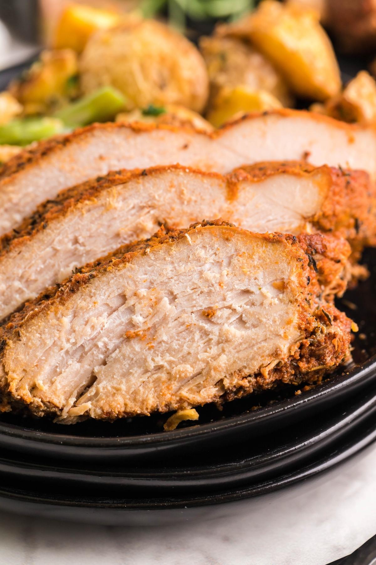 Sliced, seasoned chicken breast on a black plate with roasted potatoes in the background, reminiscent of a Slow Cooker Apple Cider Turkey Breast for an easy, flavorful meal.