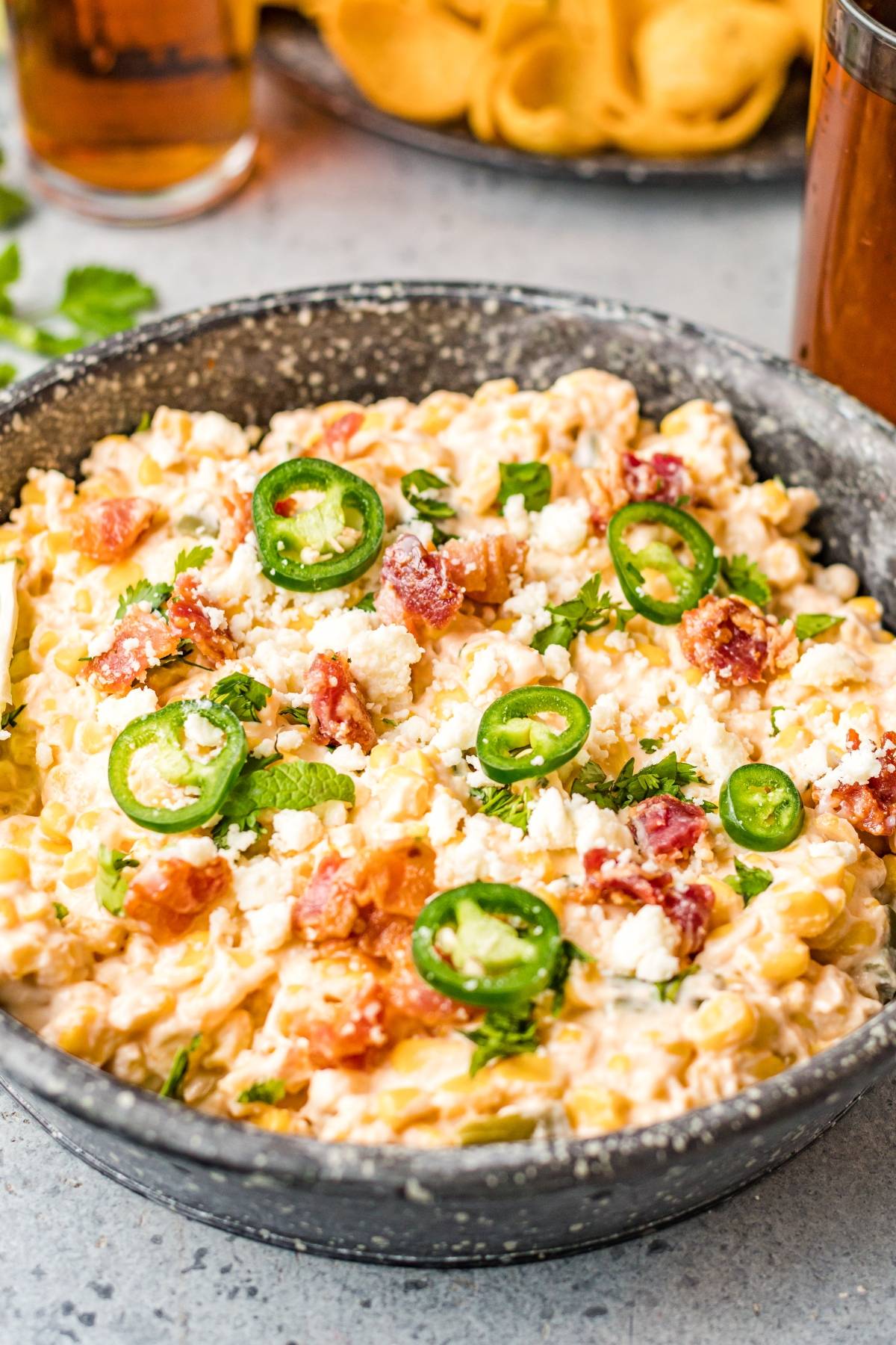 Creamy jalapeño corn dip topped with sliced jalapeños, bacon, and crumbled cheese in a black bowl—an easy street corn dip perfect for parties.