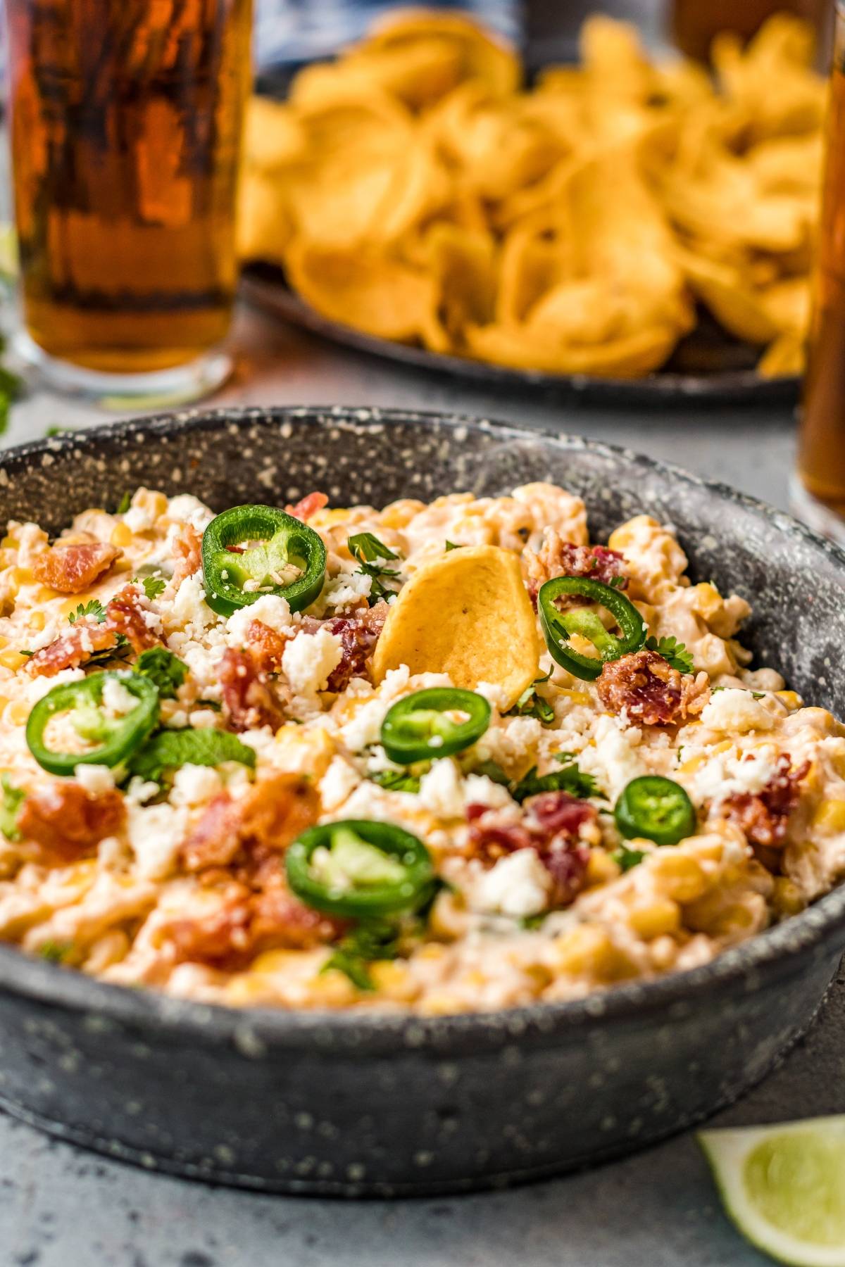 Creamy Slow Cooker Jalapeño Corn Dip topped with jalapeños, bacon, and cheese, served with a corn chip in a black bowl—a cheesy Mexican-style appetizer perfect for sharing.