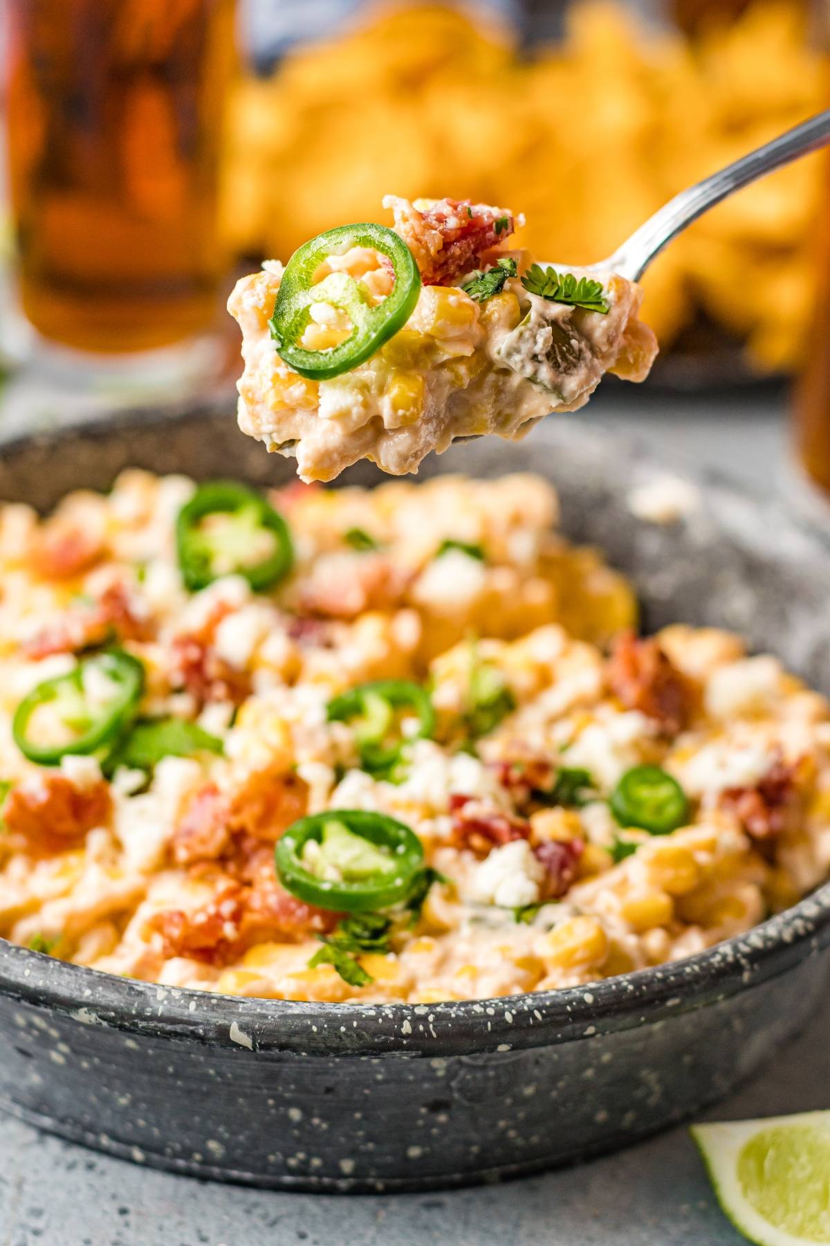 A fork holds creamy easy street corn dip topped with jalapeño slices above a bowl filled with the same dip.