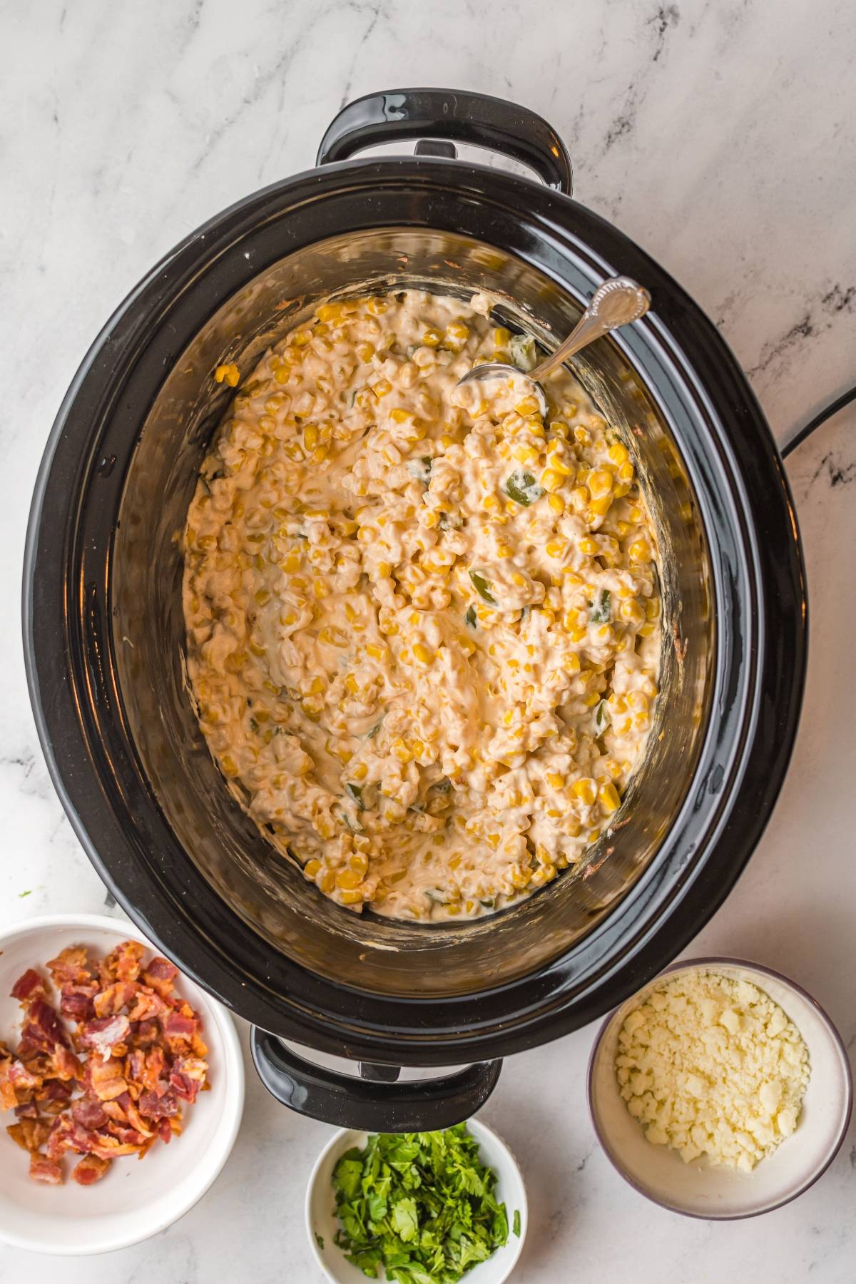 Creamy Slow Cooker Jalapeño Corn Dip, with bowls of bacon, cheese, and herbs on the side—a cheesy Mexican-style appetizer perfect for any gathering.