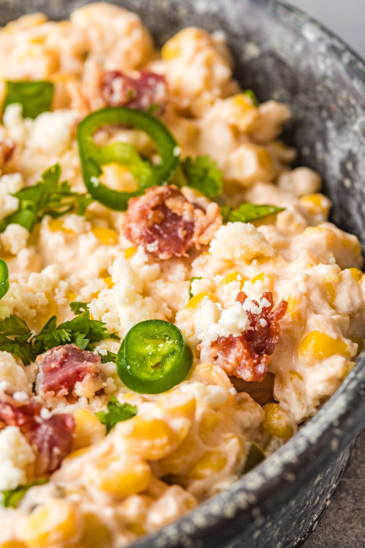 Creamy easy street corn dip topped with sliced jalapeños, cilantro, and crumbled cheese in a gray bowl.