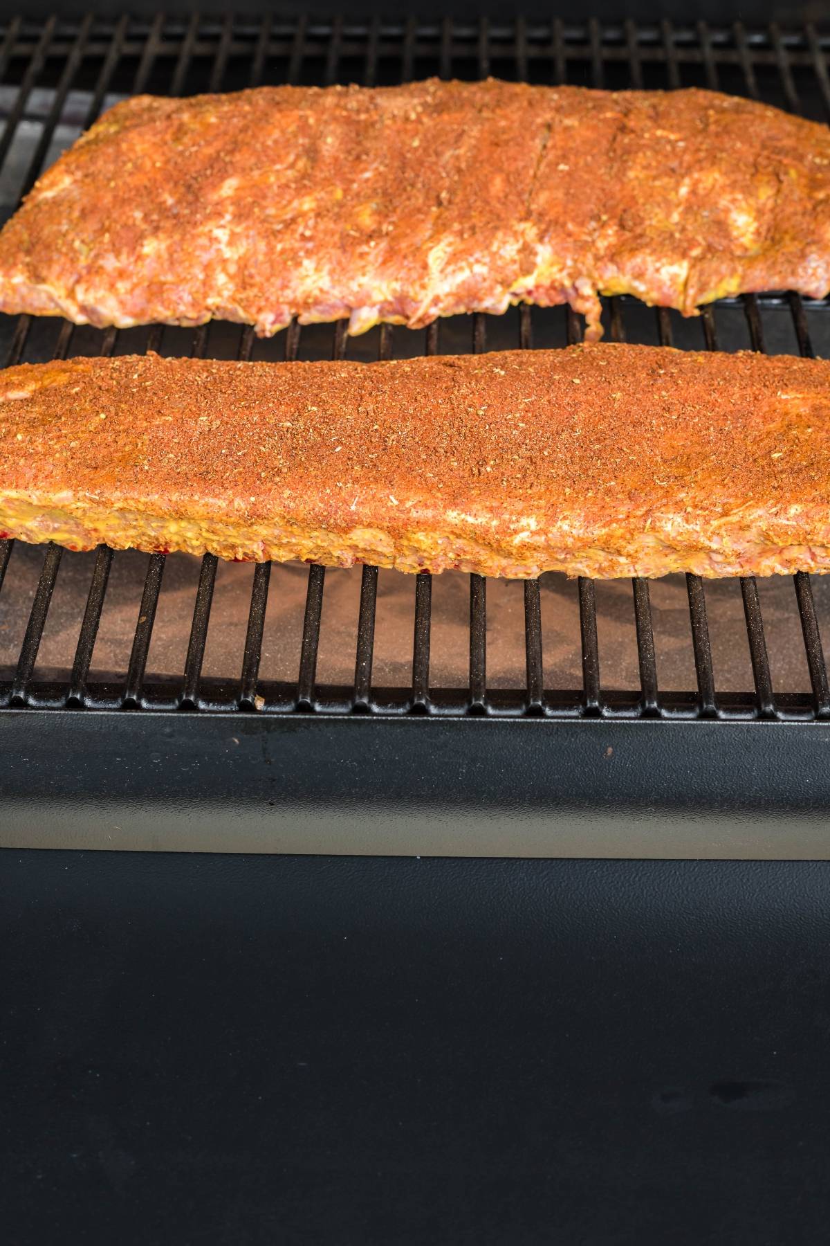 Two racks of seasoned ribs cooking on a grill with a black grate—an easy grilling recipe that's sure to become your Summer BBQ favourite.