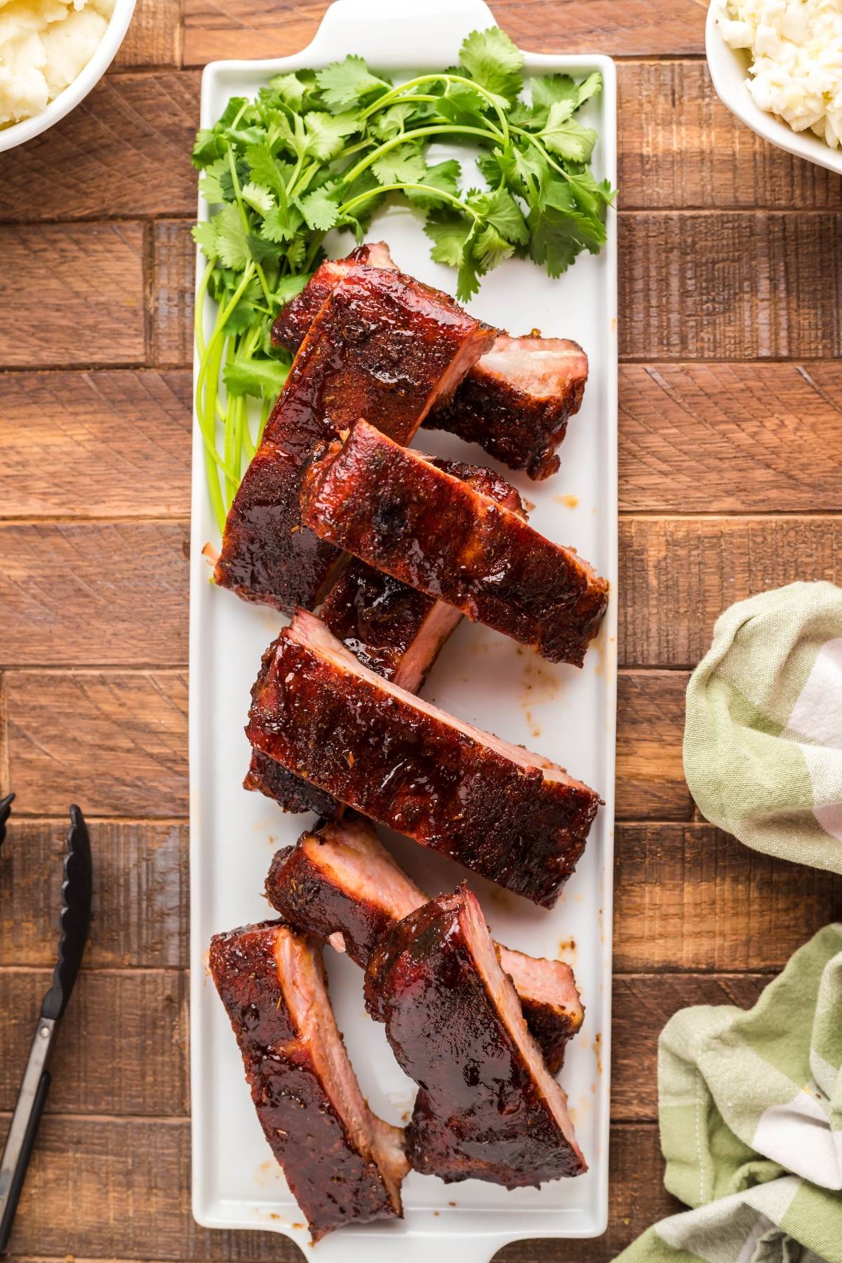 Barbecue ribs arranged on a white platter with fresh cilantro garnish, set on a wooden table—a Summer BBQ favourite and an easy grilling recipe perfect for gatherings.