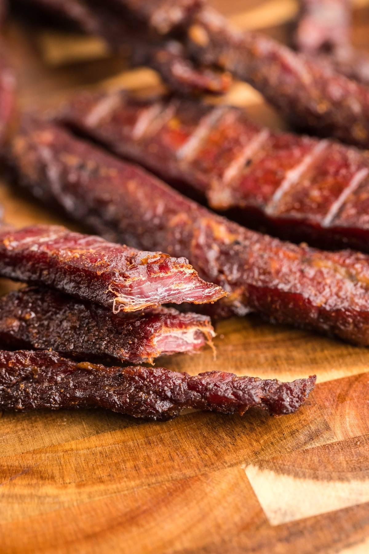 Close-up of sliced, healthy homemade beef jerky sticks on a wooden cutting board—perfect for anyone looking for gluten free paleo jerky or trying a new recipe for a smoker like a Traeger grill.