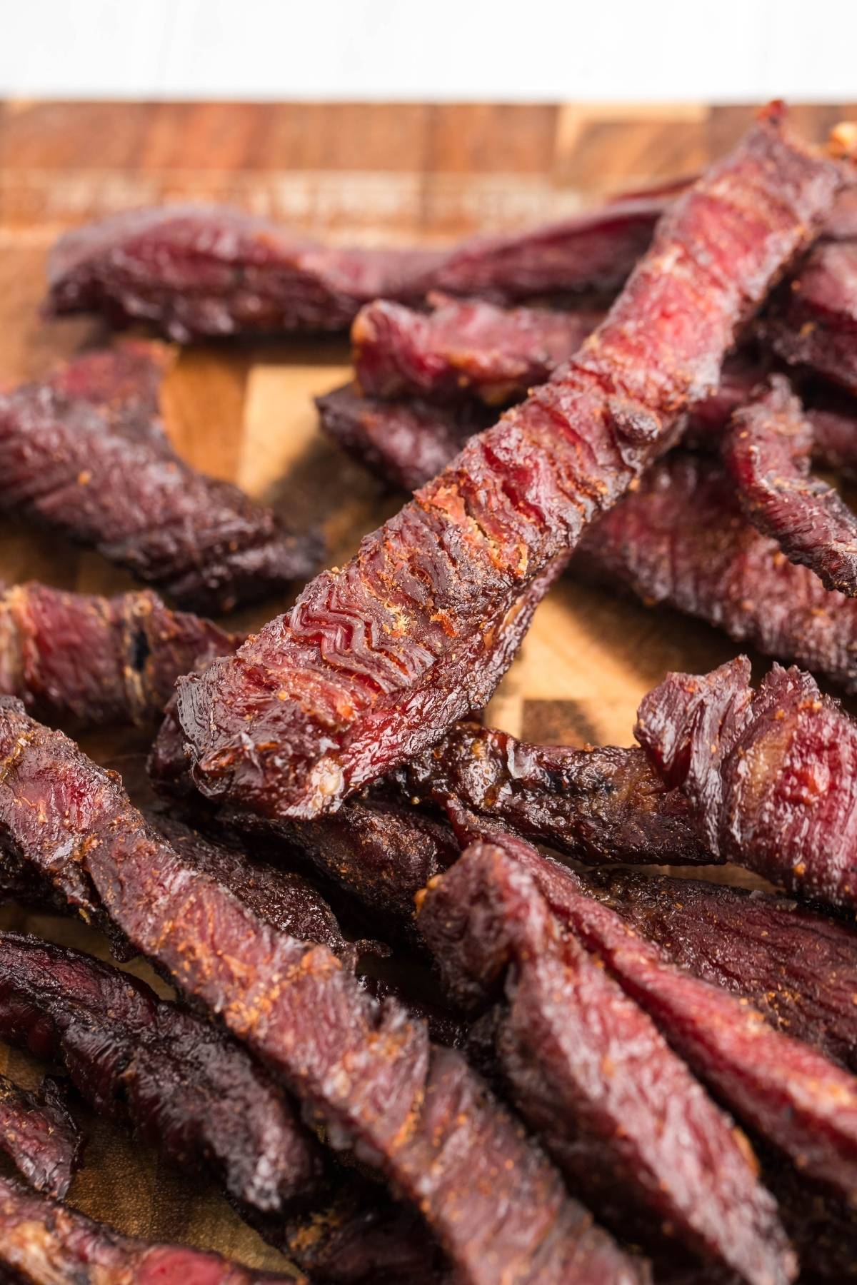 Close-up of several pieces of smoked beef jerky on a wooden surface, showcasing the results you can achieve with a recipe for a smoker like a Traeger grill.
