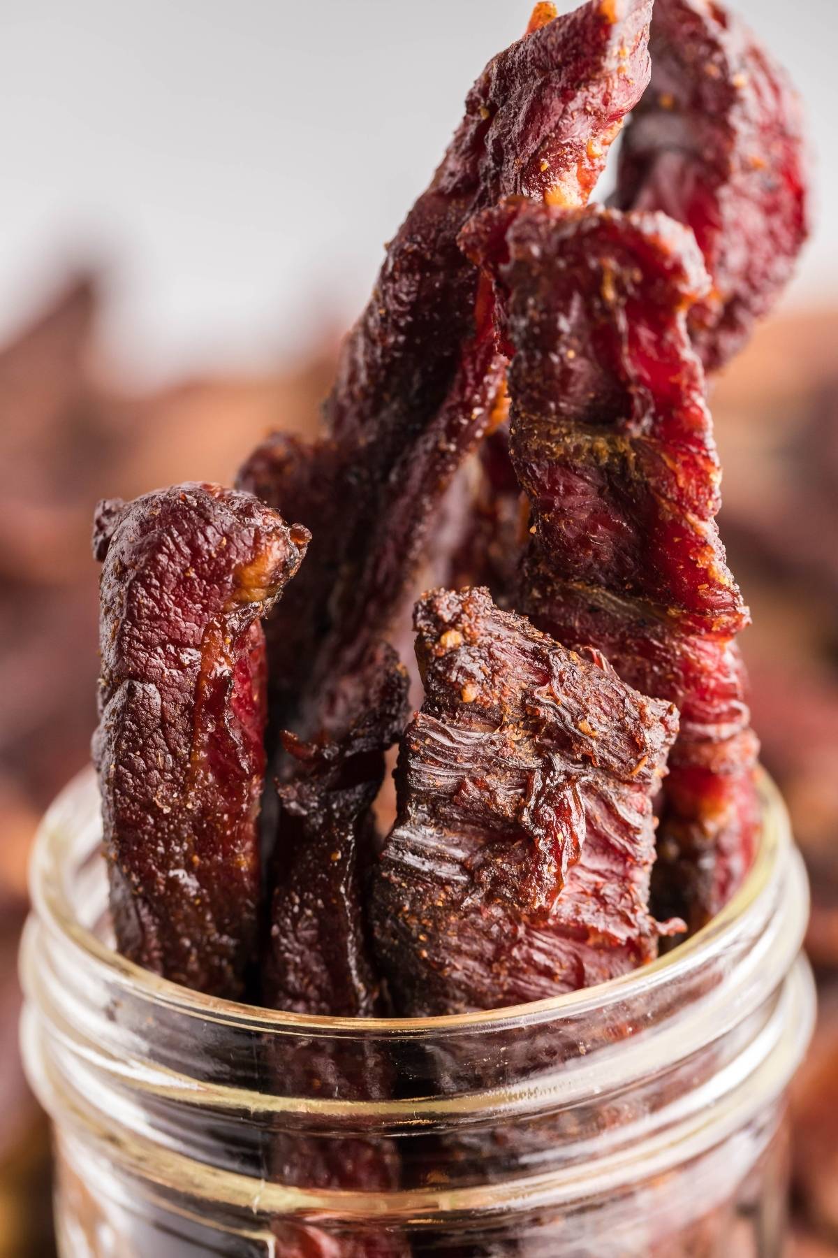 Several pieces of gluten free paleo jerky stand upright in a glass jar, showing their dark, textured surface—a perfect snack for those curious about how to make smoked beef jerky at home.
