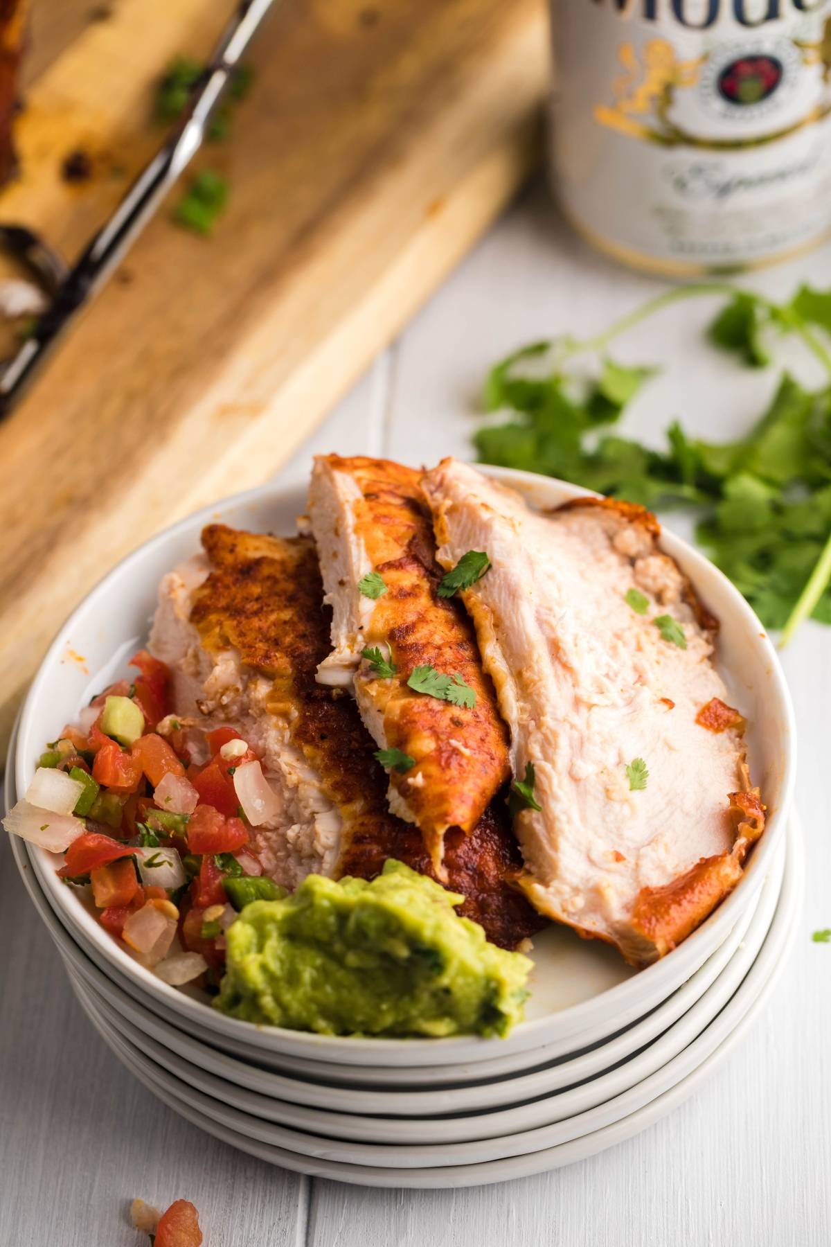 Sliced grilled chicken breast with pico de gallo and guacamole on a white plate, garnished with cilantro and drizzled with Mexican BBQ sauce.