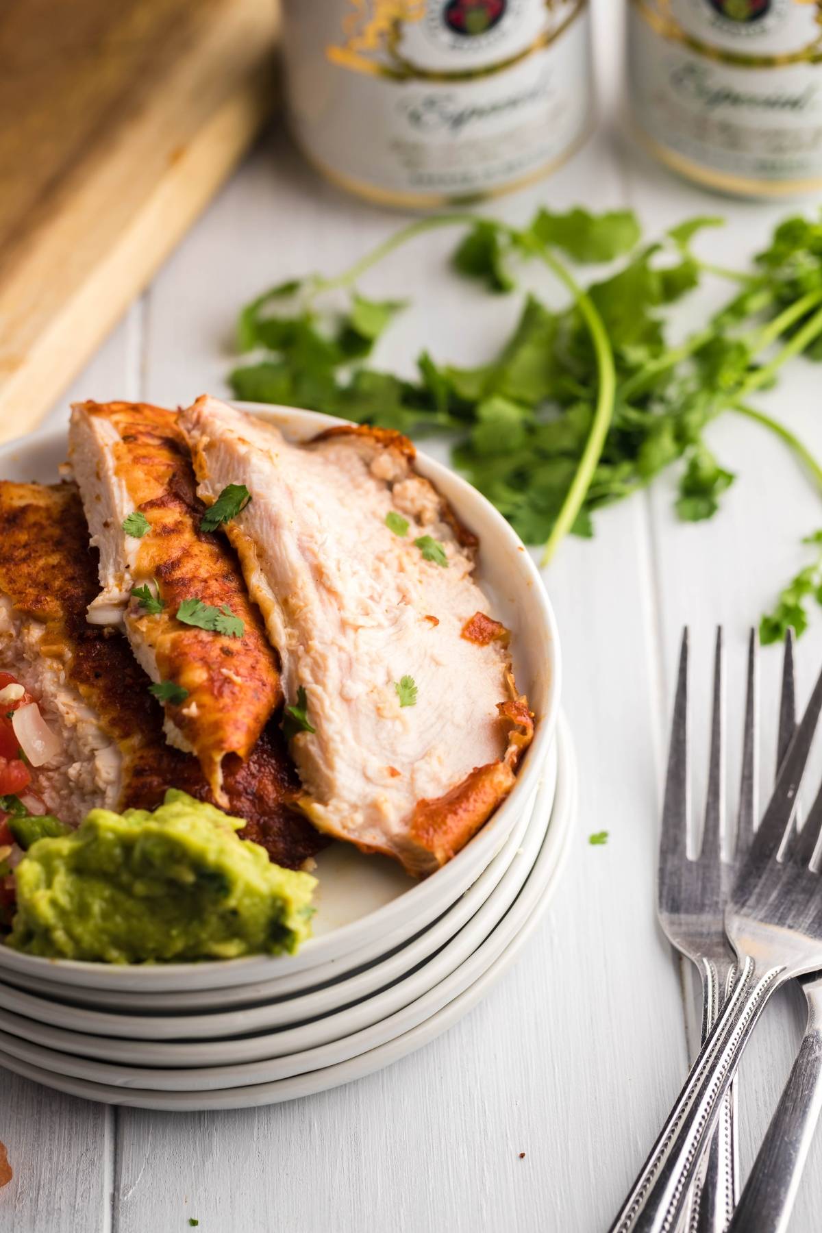 Sliced grilled chicken, inspired by a classic grilled chicken recipe with guacamole and cilantro, served on a small white plate, with forks and herbs nearby.